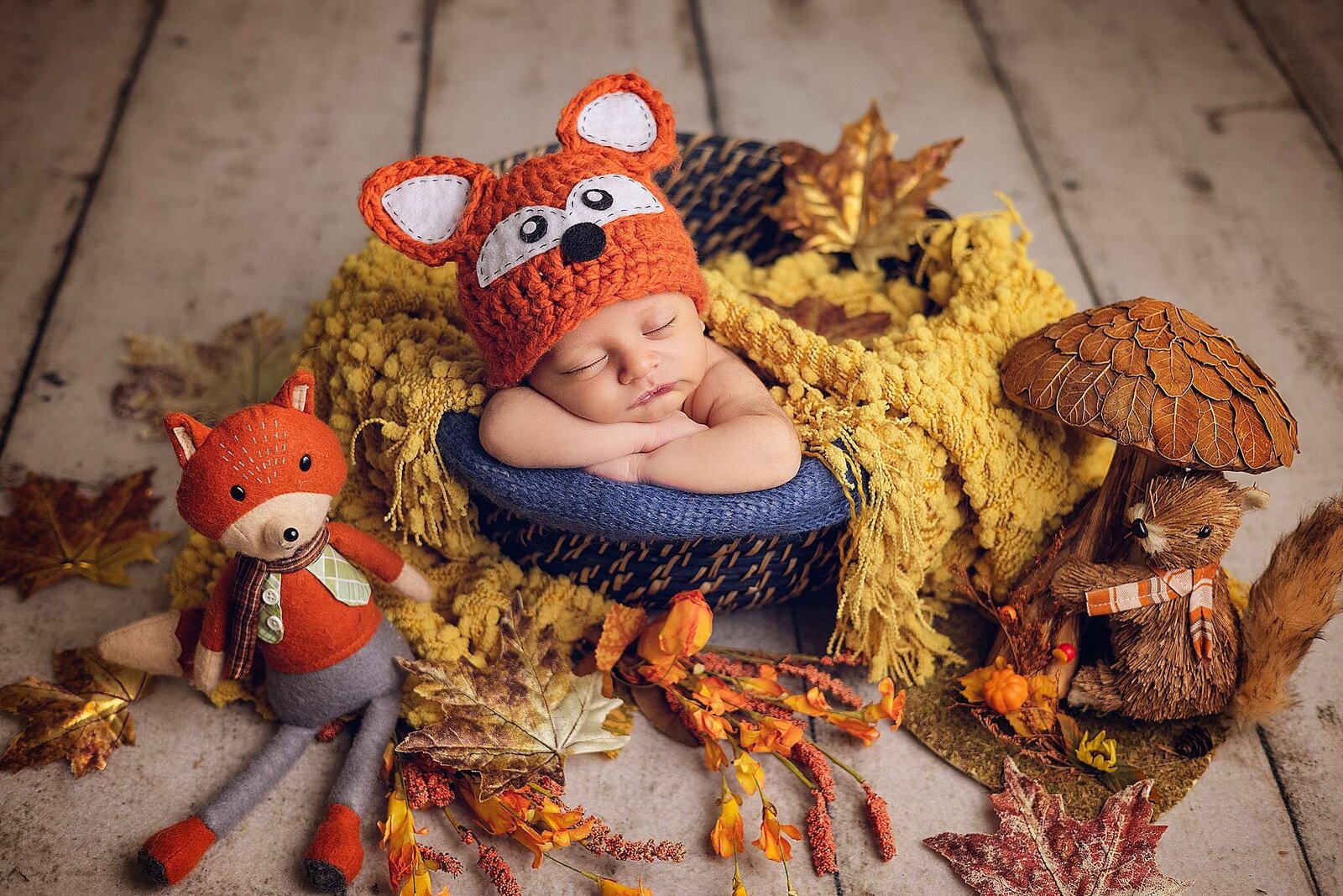A newborn boy in a fox hat nestled among vibrant autumn leaves, captured by Bia Schaefer, Windermere newborn photographer.