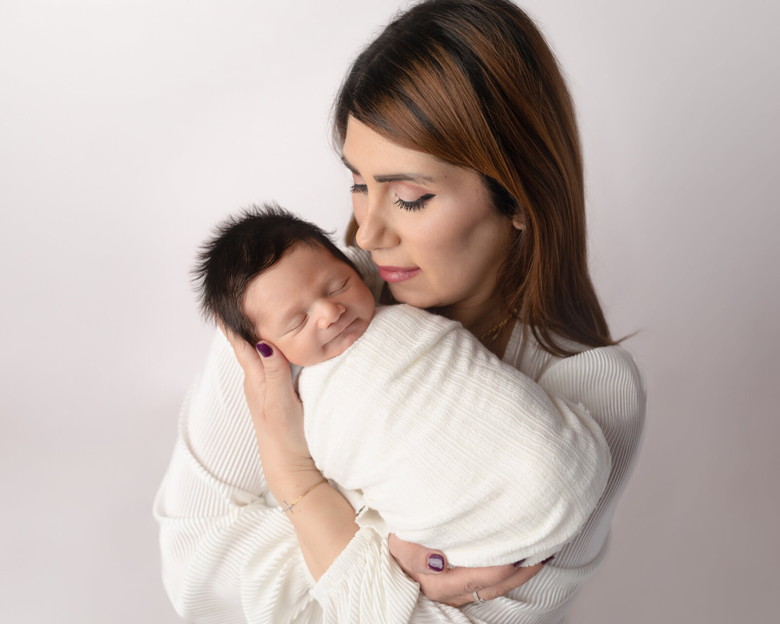 mom holding newborn baby boy wrapped in white for studio portraits