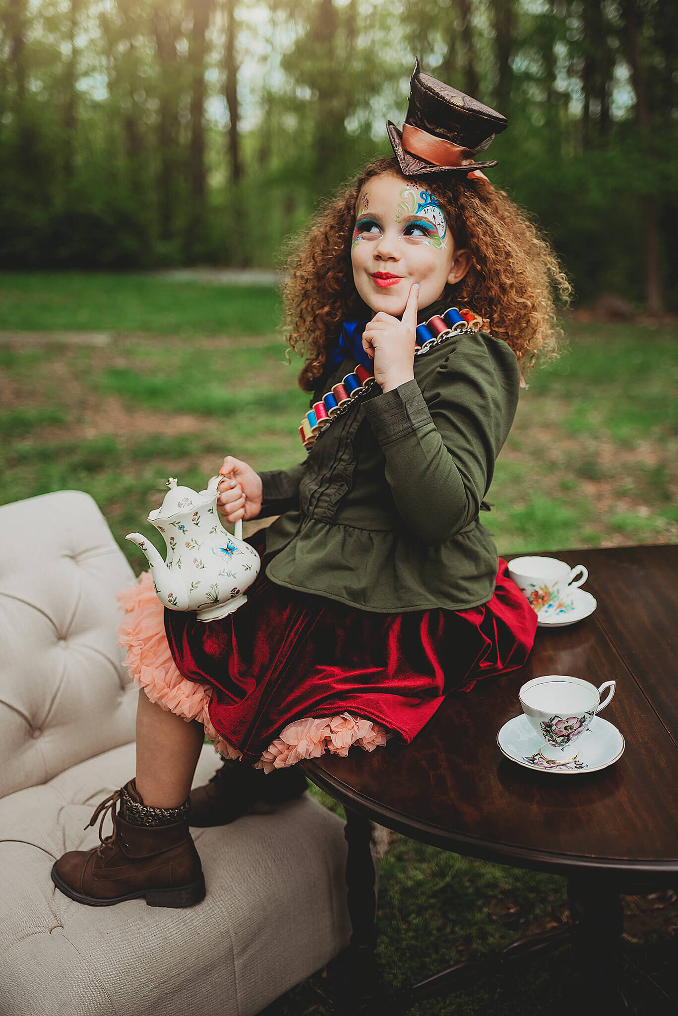 Girl with orange hair and face makeup sitting on table with tea set