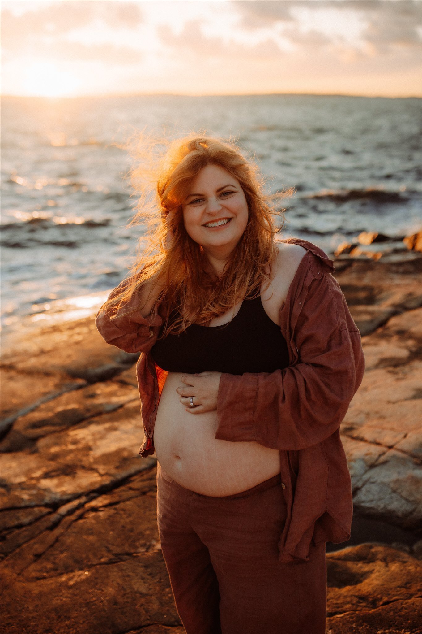 en gravid mamma står på klippor med vinden i håret och skrattar
