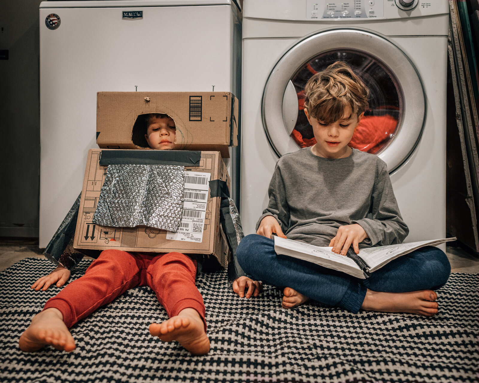 Two boys sitting in front of washer and dryer