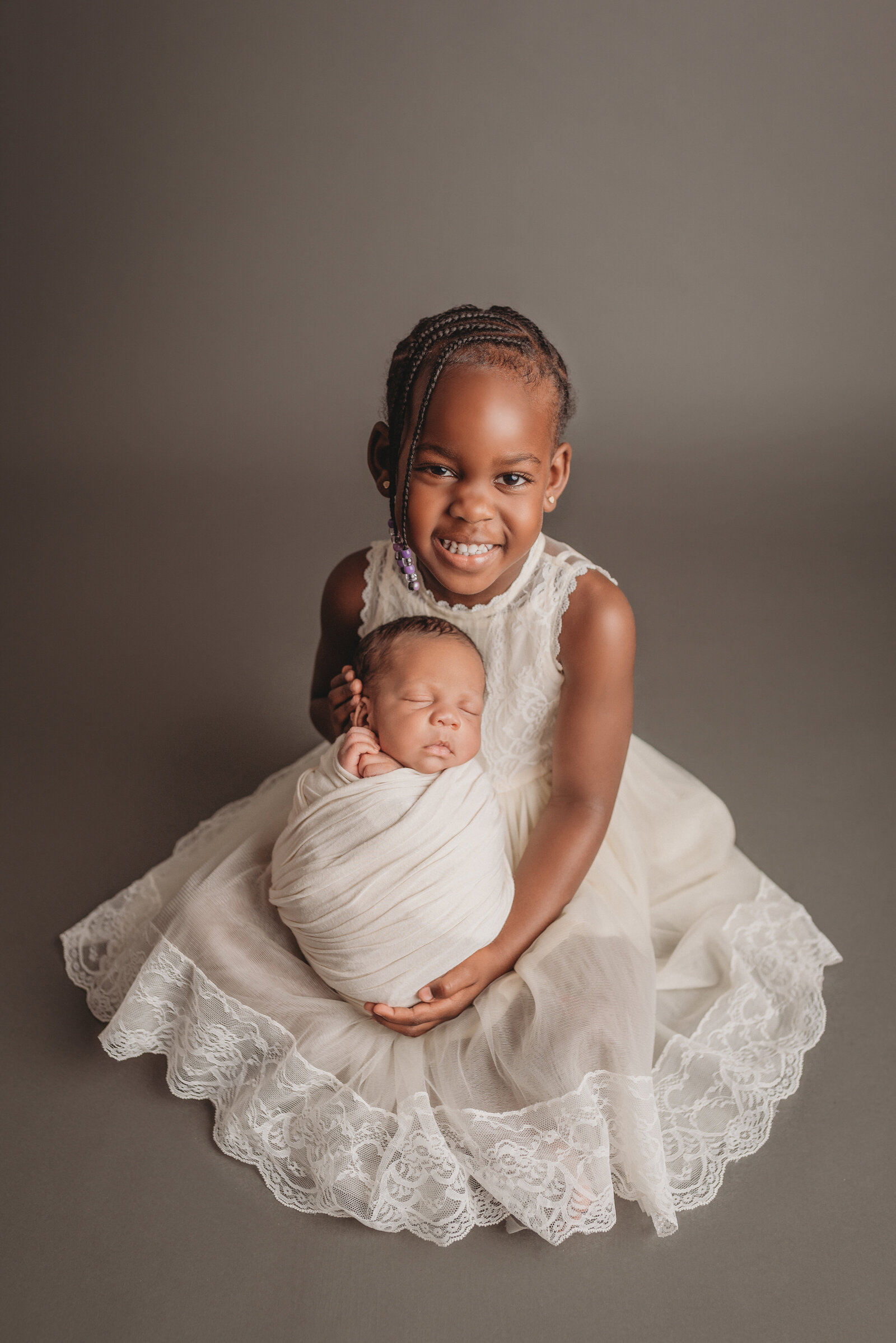 Sisters, 4 year old and newborn, portrait with big sister holding newborn sister under the head and bottom while smiling