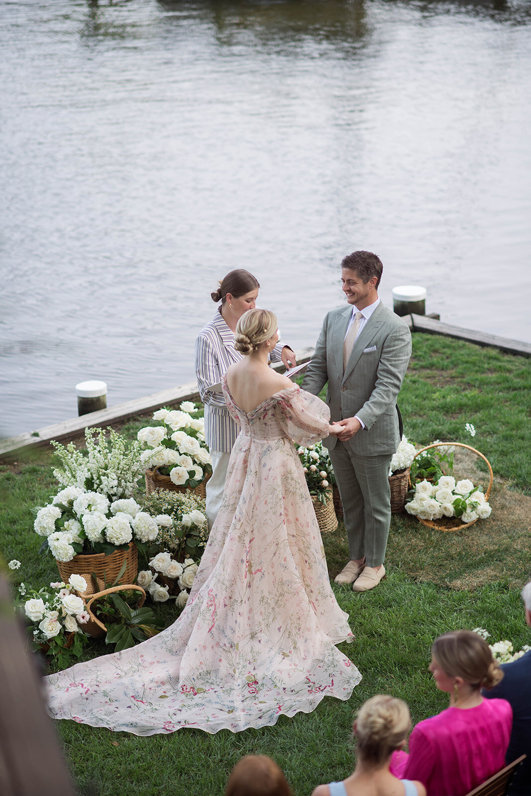 Bride and groom ceremony photograph standing in front of wicker baskets filled with white garden roses, white hydrangea, blush peonies, and blush butterfly ranunculus.