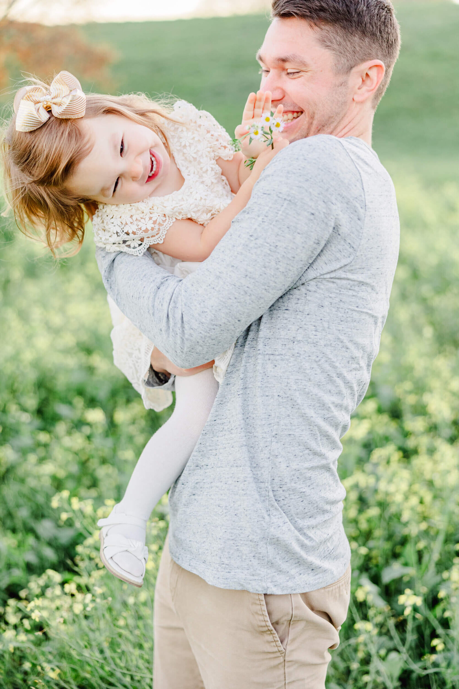 Dad and the daughter he's holding laugh in a flower field