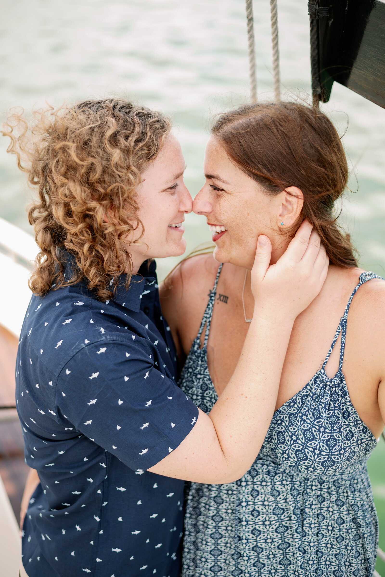 engaged couple about to kiss. One woman has her hand on the others neck, fingers just under her ear gently. Both are smiling