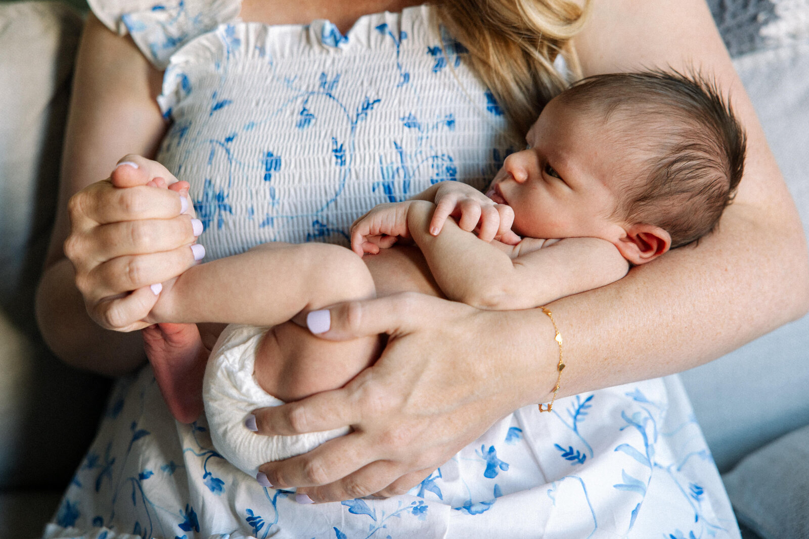 overhead photo of newborn baby girl in star onesie laying on a sheet with peach colored paint mark pattern and mom's hand reaching for her hand