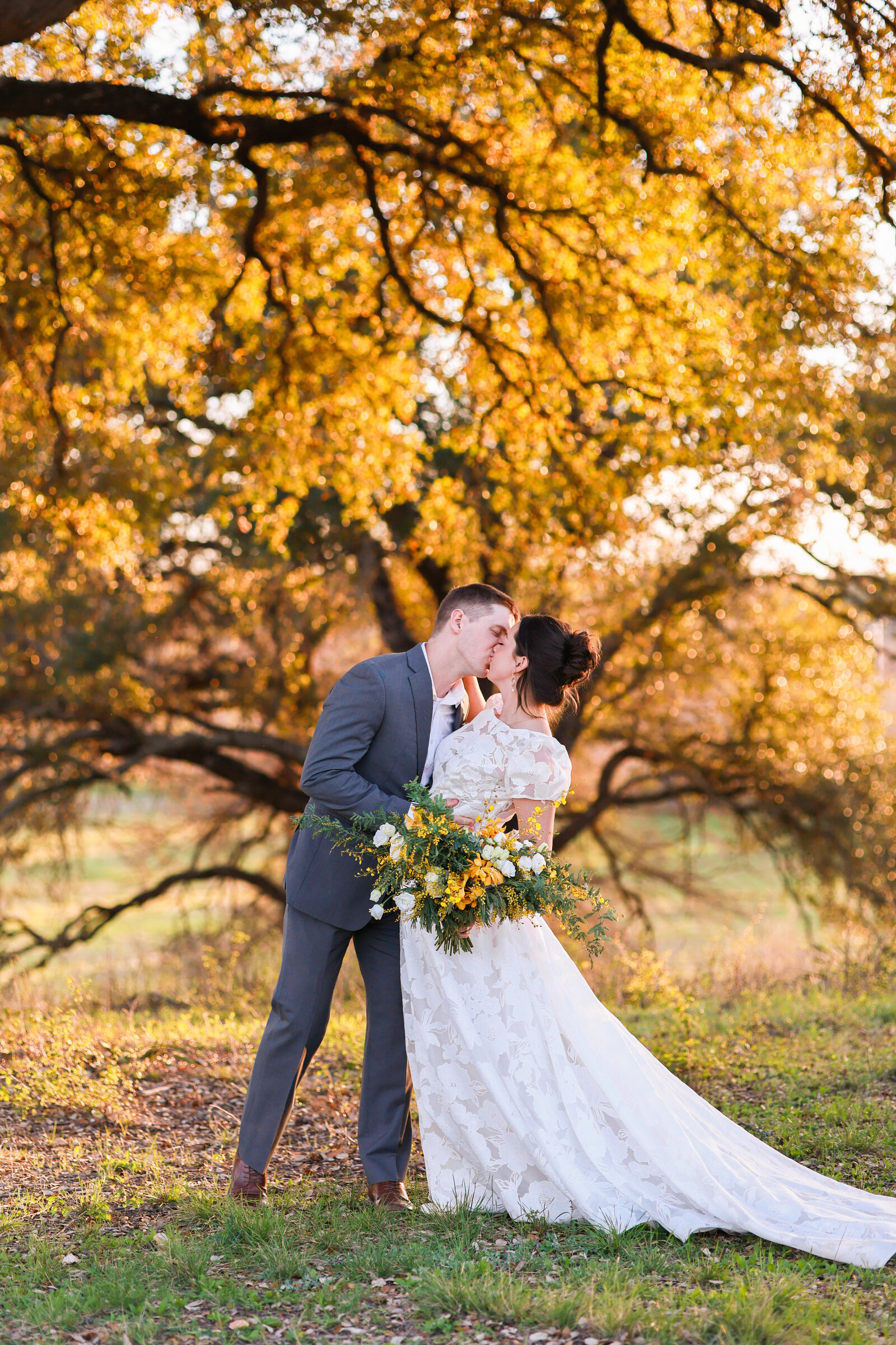 bride and groom kissing with yellow florals at Hewitt Oaks in Austin Texas by AustinTexas Wedding Photographer Amanda Richardson Photography