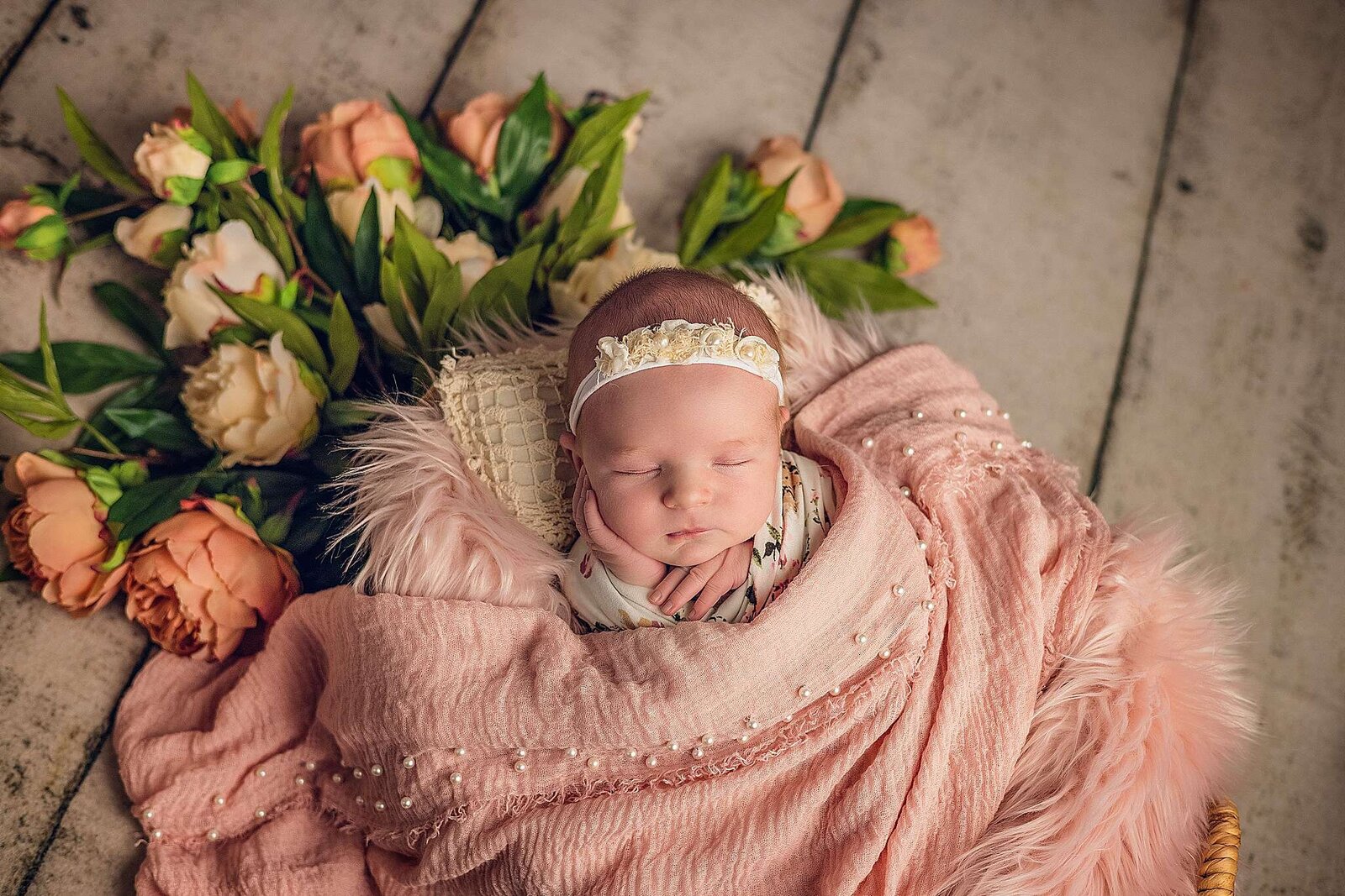A peaceful newborn girl sleeps in a flower-adorned basket, captured by Bia Schaefer, Orlando's expert newborn photographer.