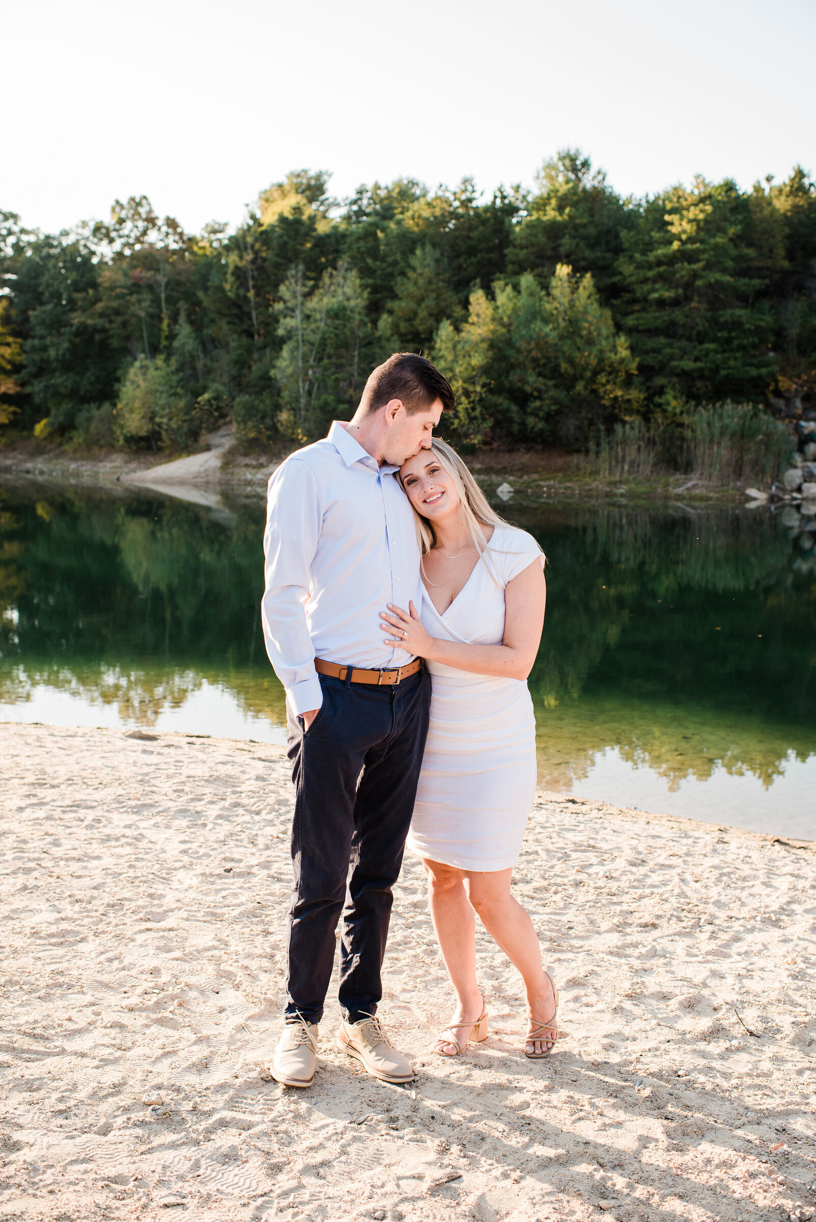 couple standing in front of pond kiss on forehead