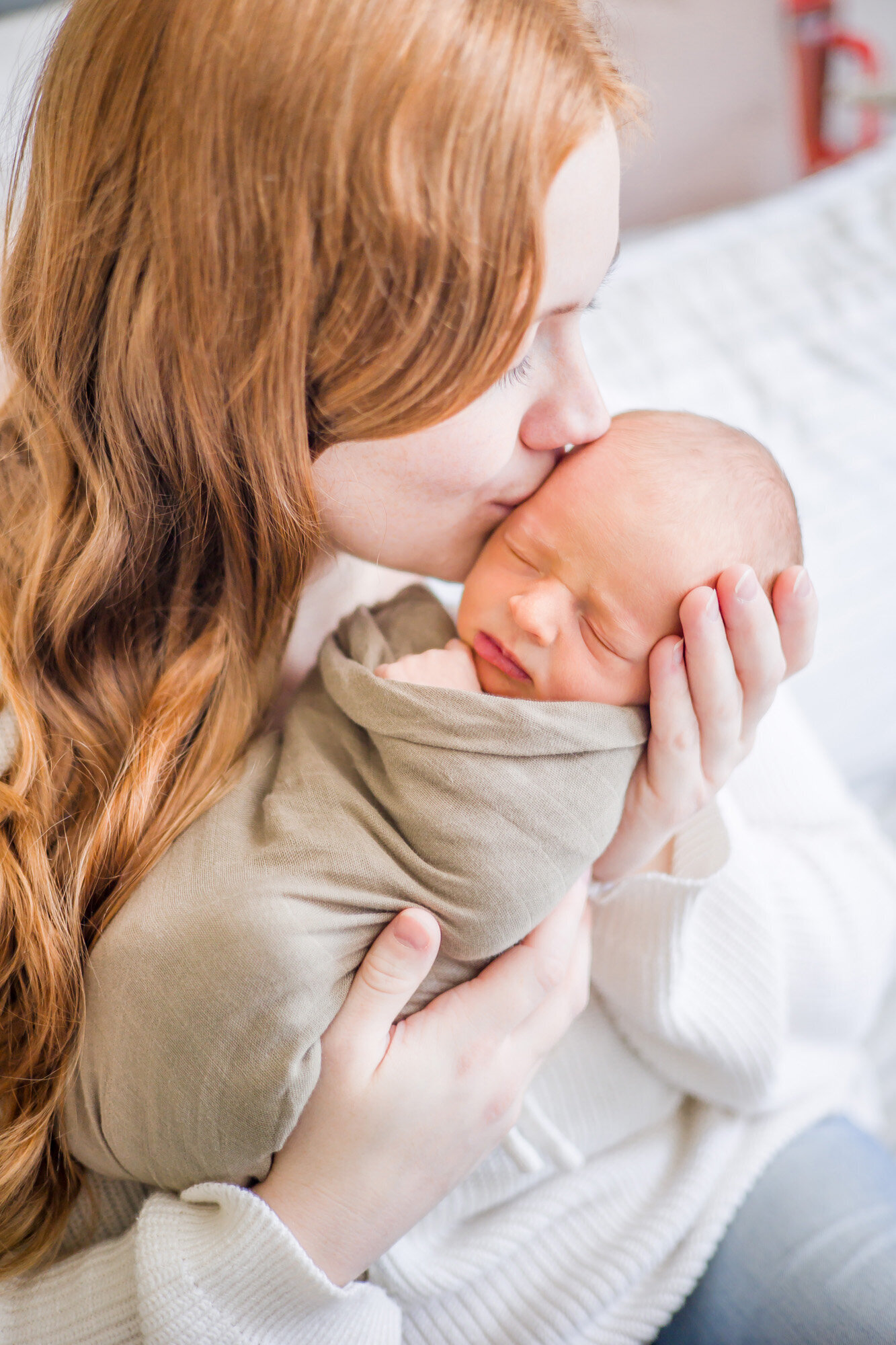 redhaired mother kissing her newborn son wrapped in a green swaddle during newborn session