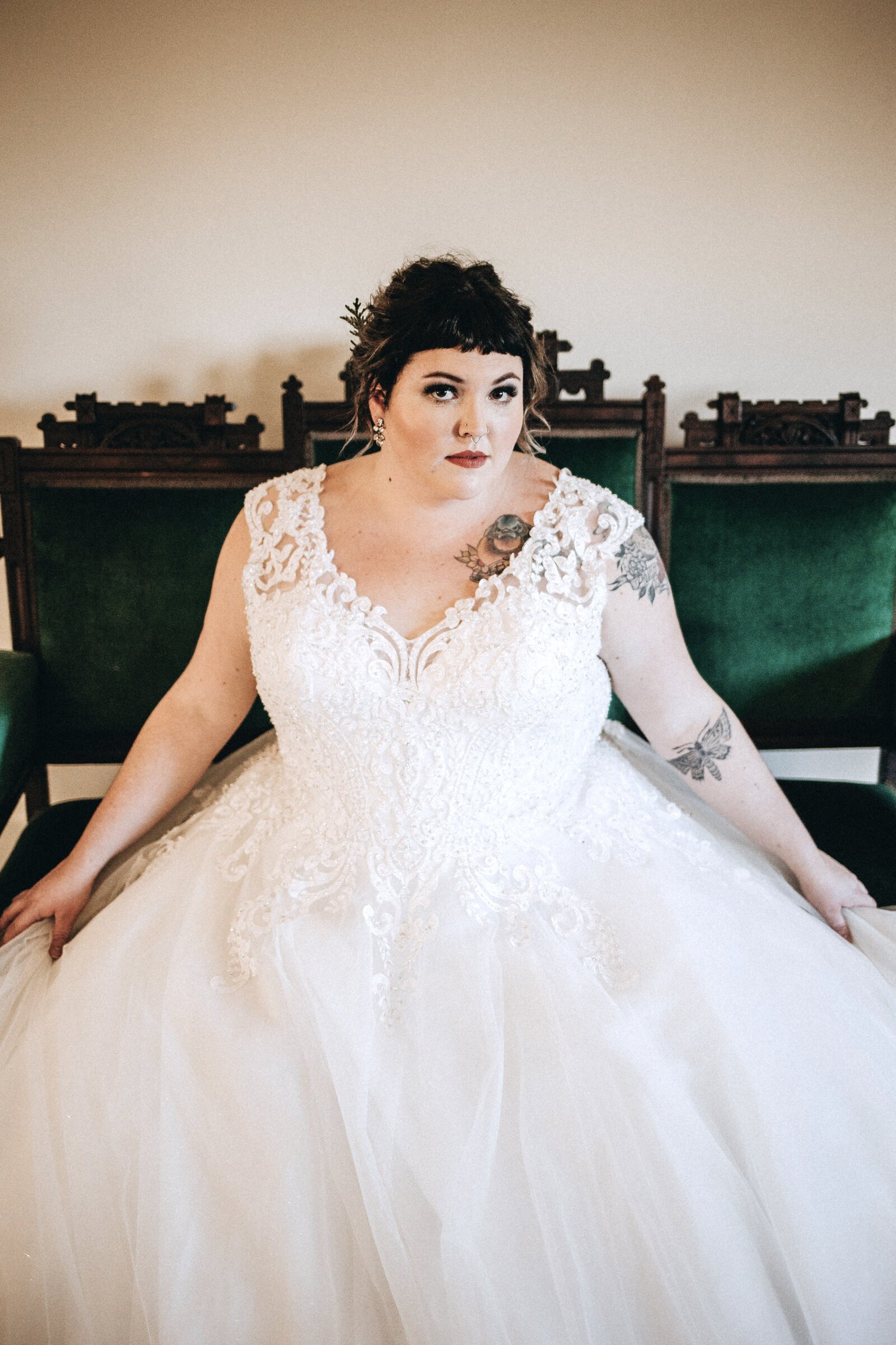 Bride looking at camera tattoo lace dress green velvet chairs