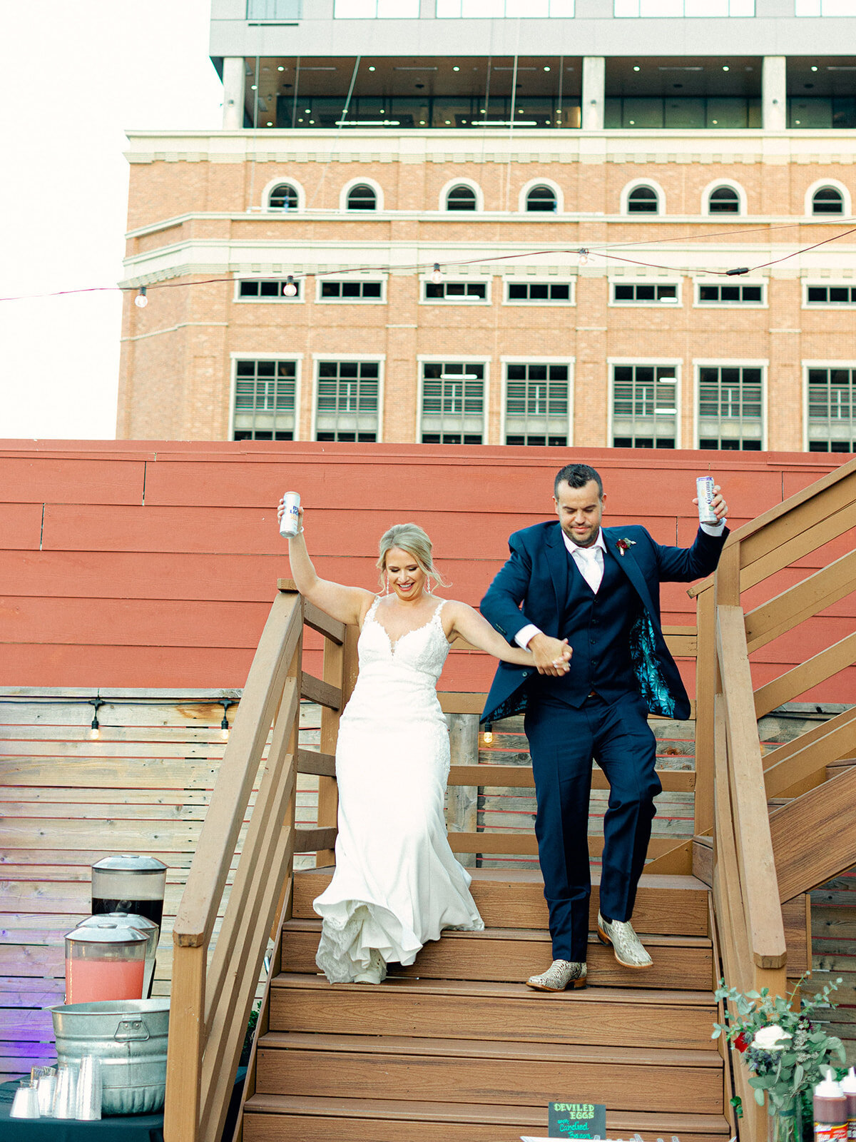 Bride and groom holding drinks and walking down a ramp