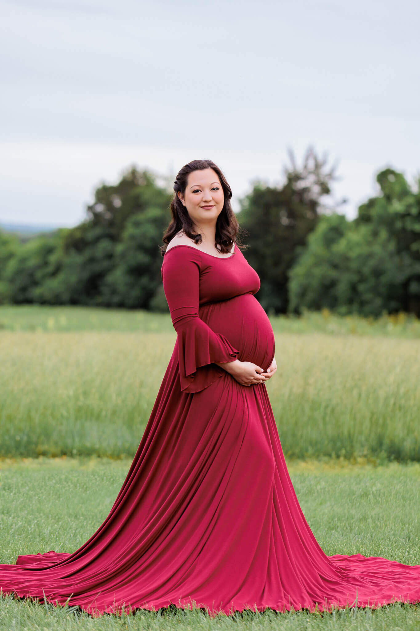 A beautiful mother-to-be posing in a field in Manassas in a red dress.