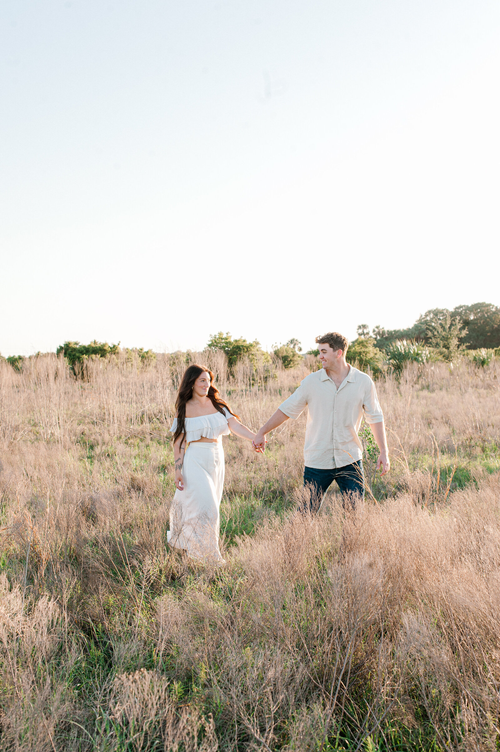 Couple holding hands and walking through a tall grass field during their photo session with an Orlando couples photographer