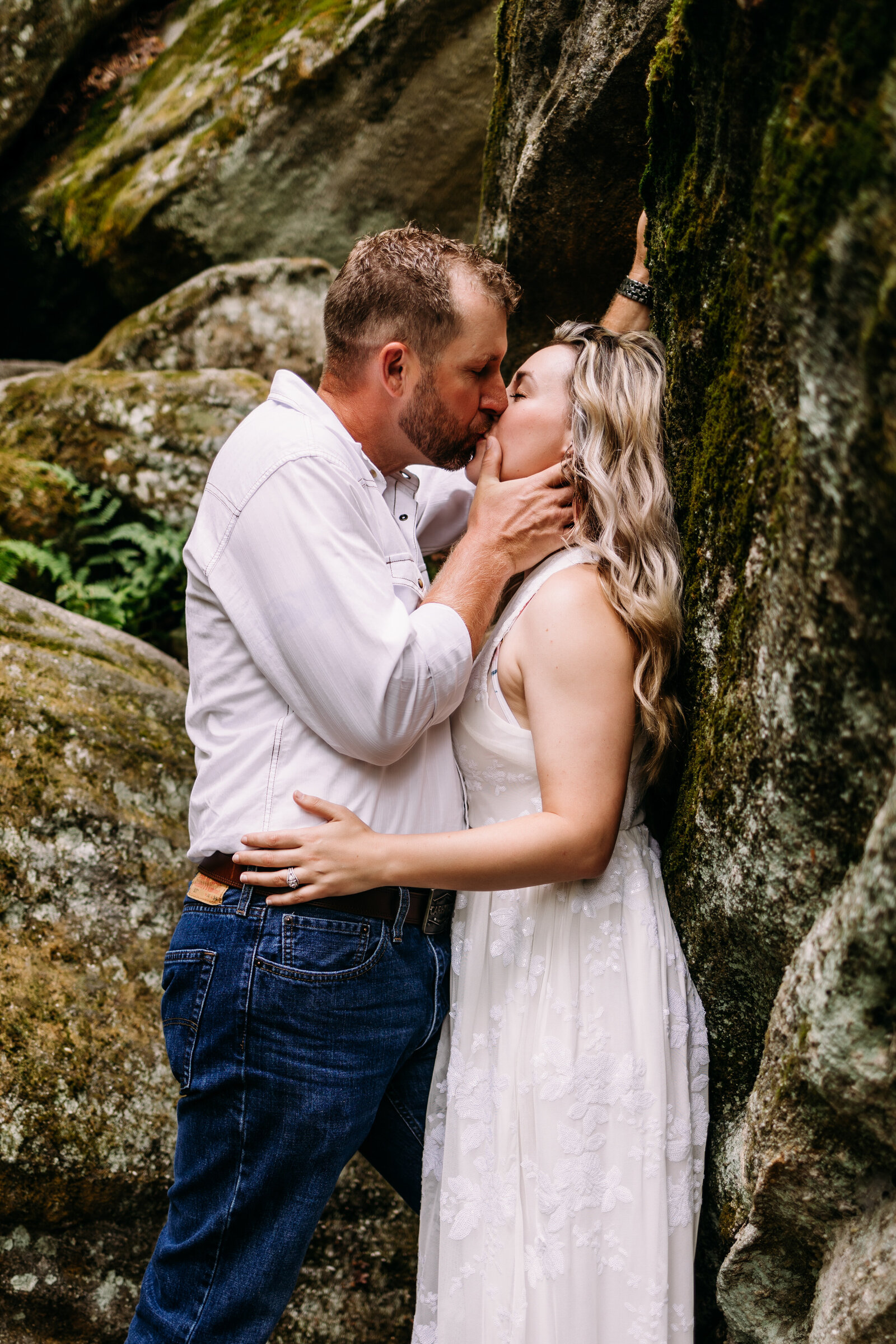 Man intimately kisses his fiancé up against a stone rock formation