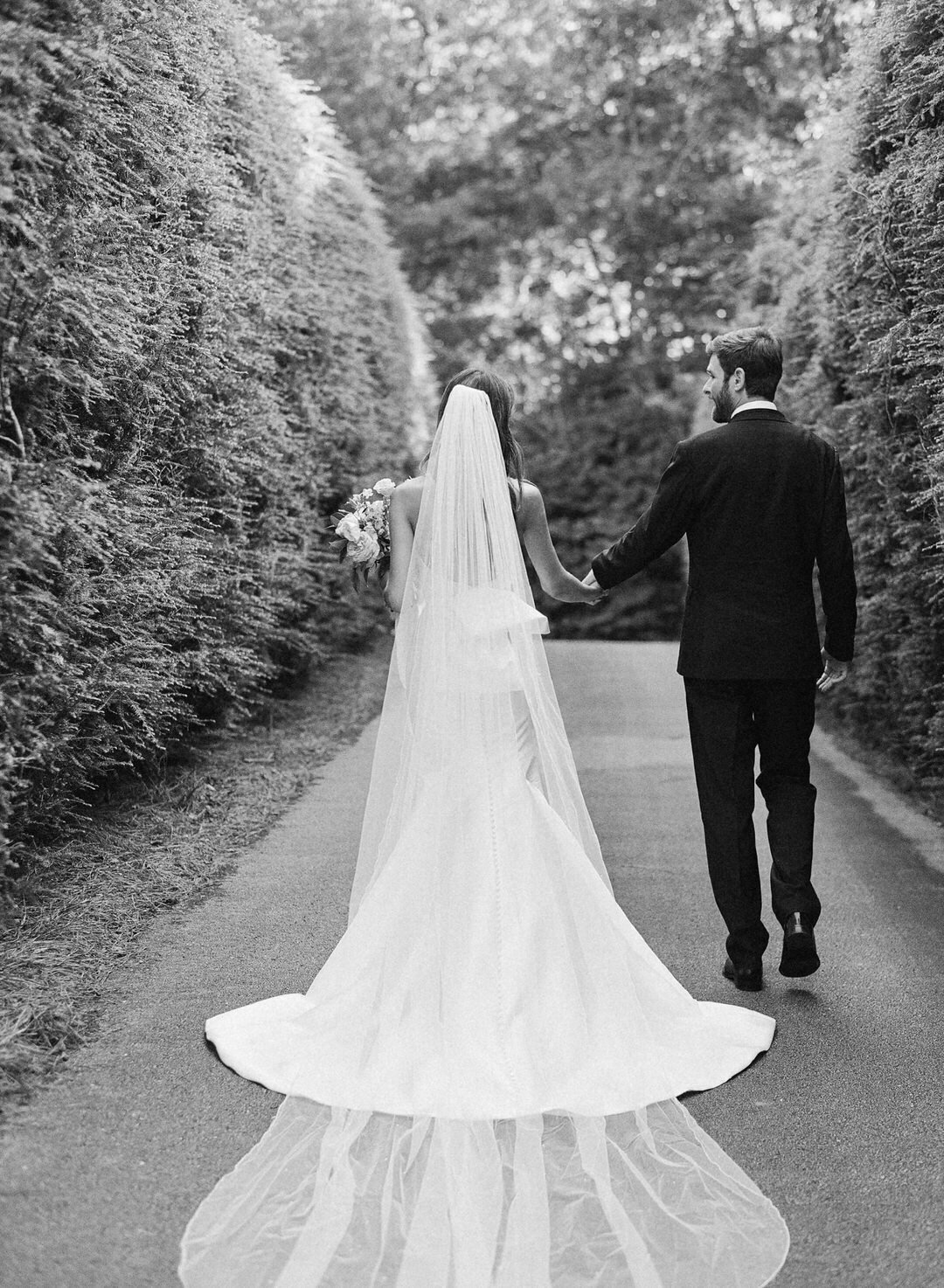 Black and White of bride and Groom Holding hands walking through hedges at The Farm at Old Edwards Inn