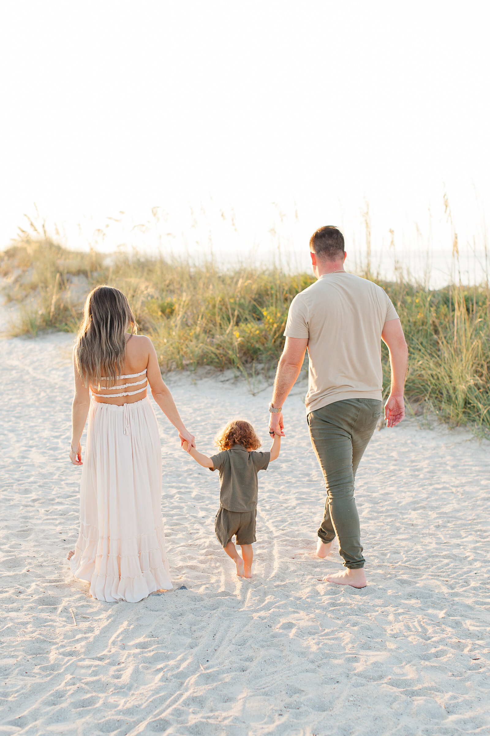 Pregnant family holding hands and walking on the beach at sunrise