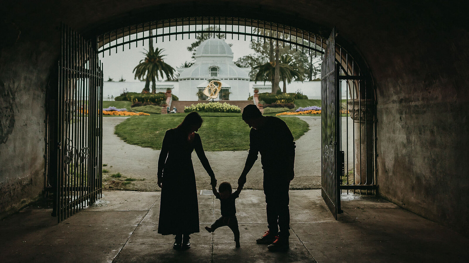 Silhouette of family holding hands and toddler walking at conservatory of flowers in SF
