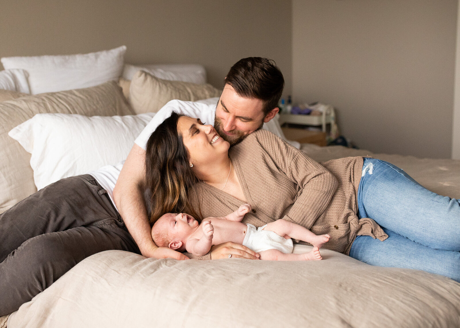 New parents snuggle on bed while taking in the first few days with newborn. Portland Newborn Photographer.