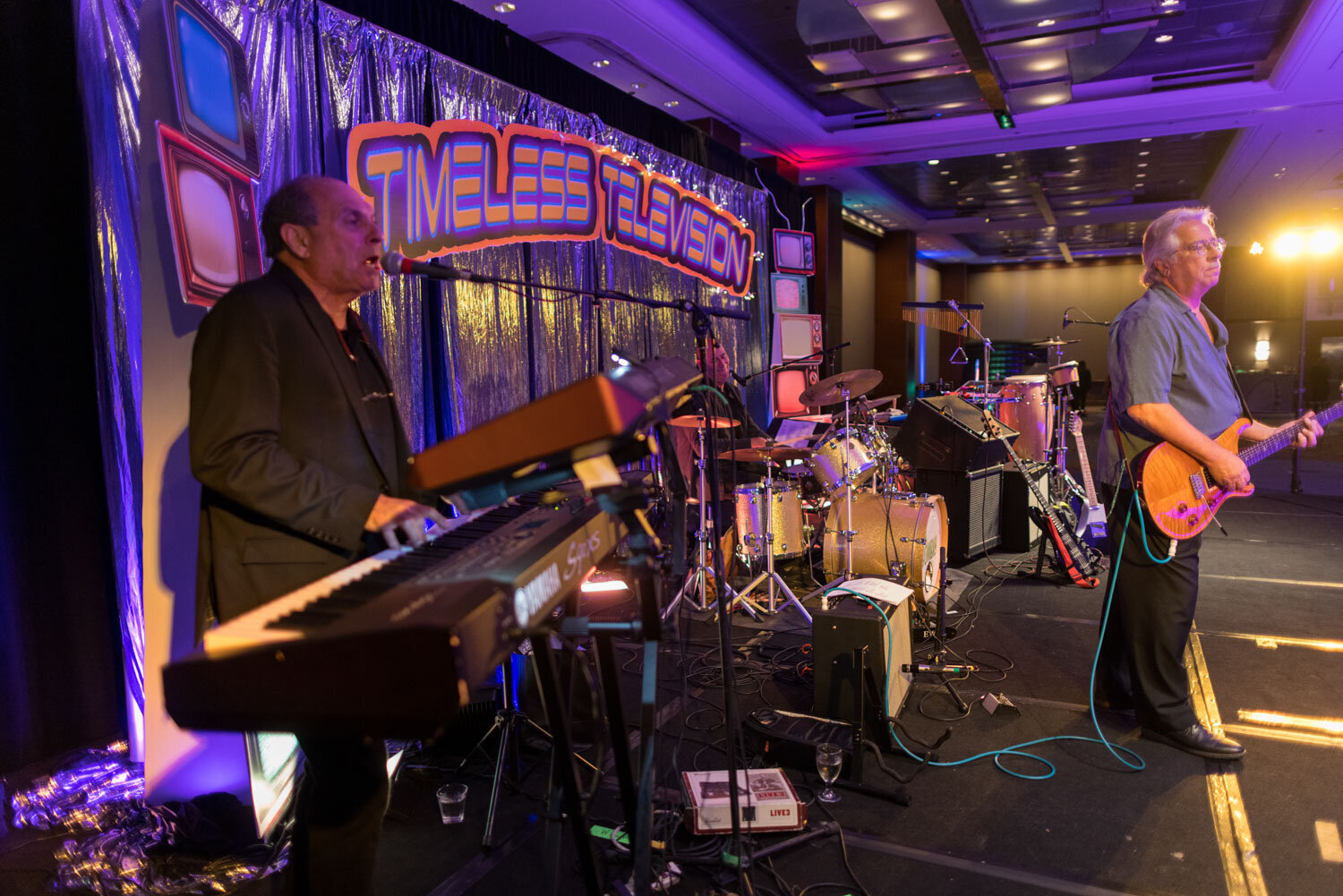 Live band setup with keyboards and drums under a "Timeless Television" banner