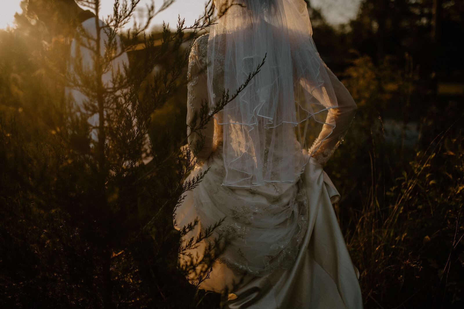 bride running through field holding wedding dress sunlight creating silhouette  through veil