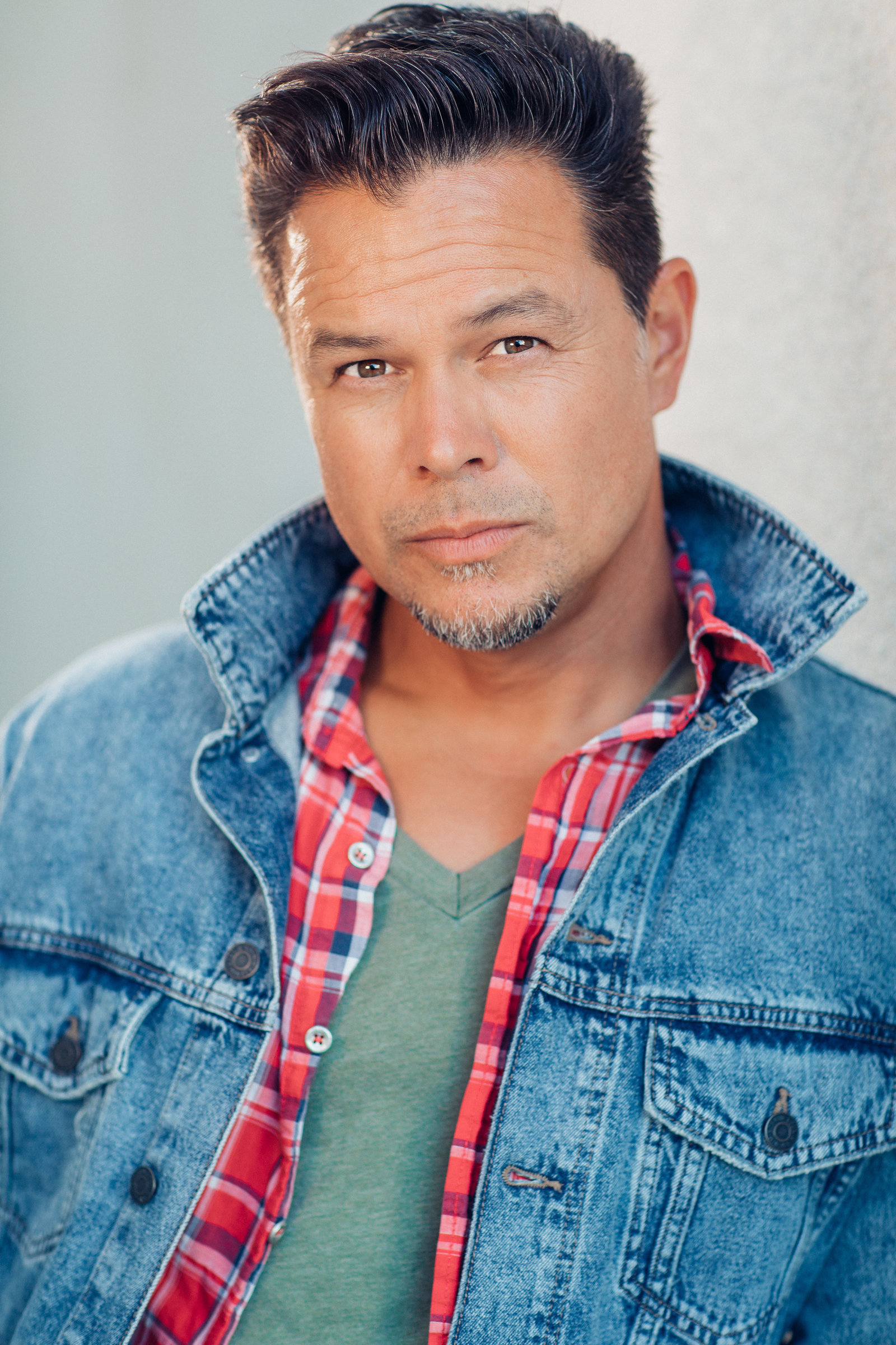 Headshot Photo Of Man In Outer Blue Denim Jacket And Inner Checkered Polo