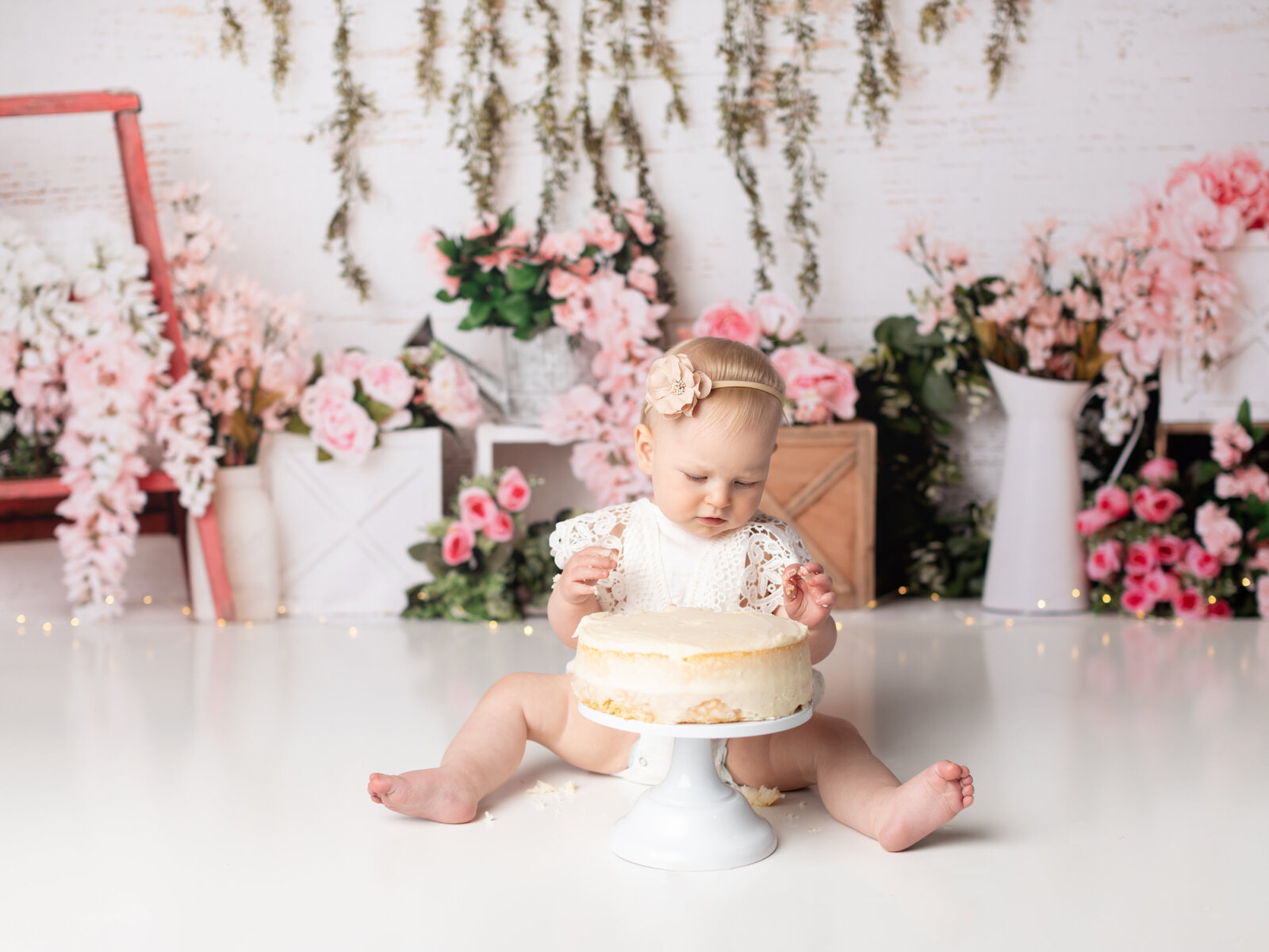 girl in white lace romper for first birthday cake smash