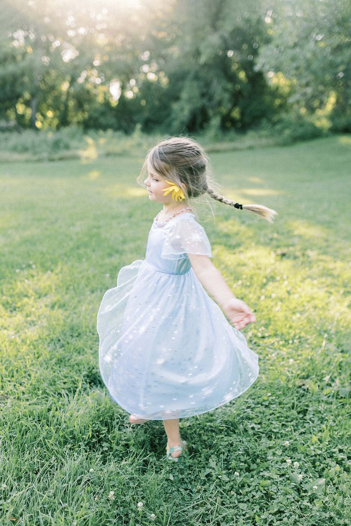 A young girl in a blue dress twirling in a field at Turtle River State Park during a sunset family session. 