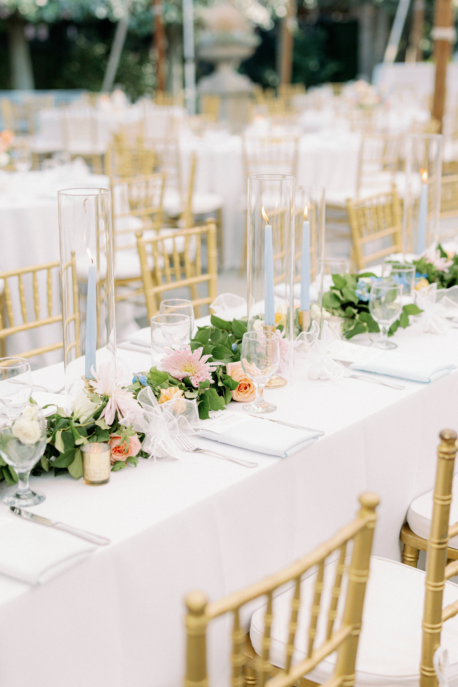 A wedding reception at the Gibbes Art Museum in Charleston, SC with gold chairs, white tablecloths, blue candles, and pink flowers