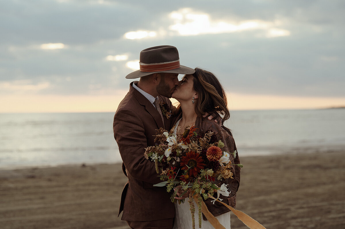 Bohemiskt brudpar kysser varandra på stranden