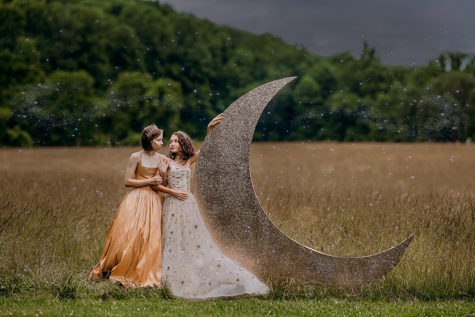 Two girls in gold gowns standing next to giant crescent moon in a field at night in Jerusalem Mill in Kingsville Maryland