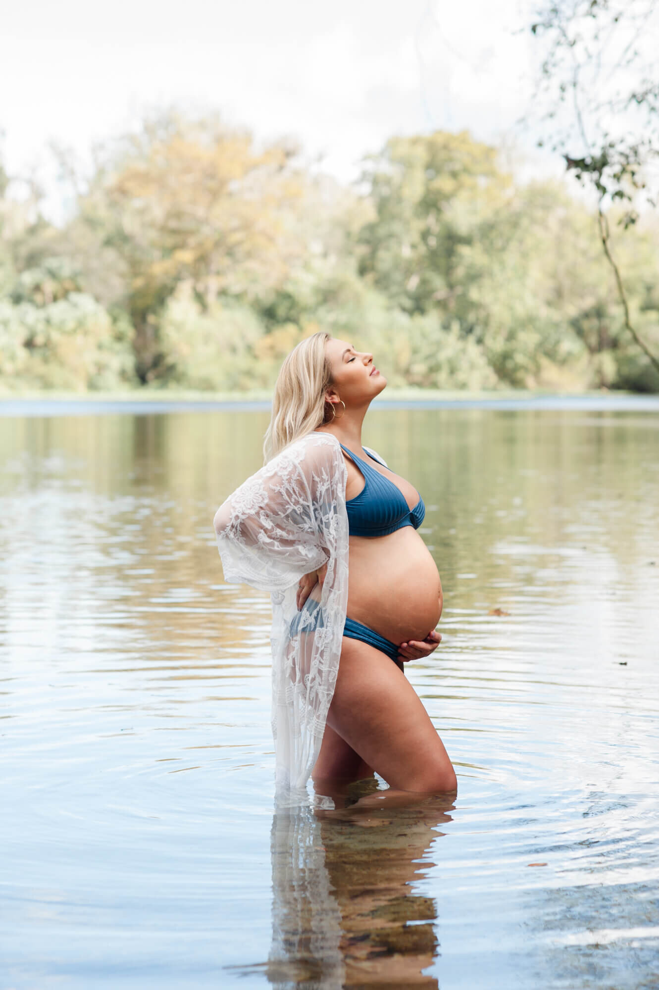 Beautiful mom standing in the spring water looking up toward the sky and holding her belly with such beauty of motherhood