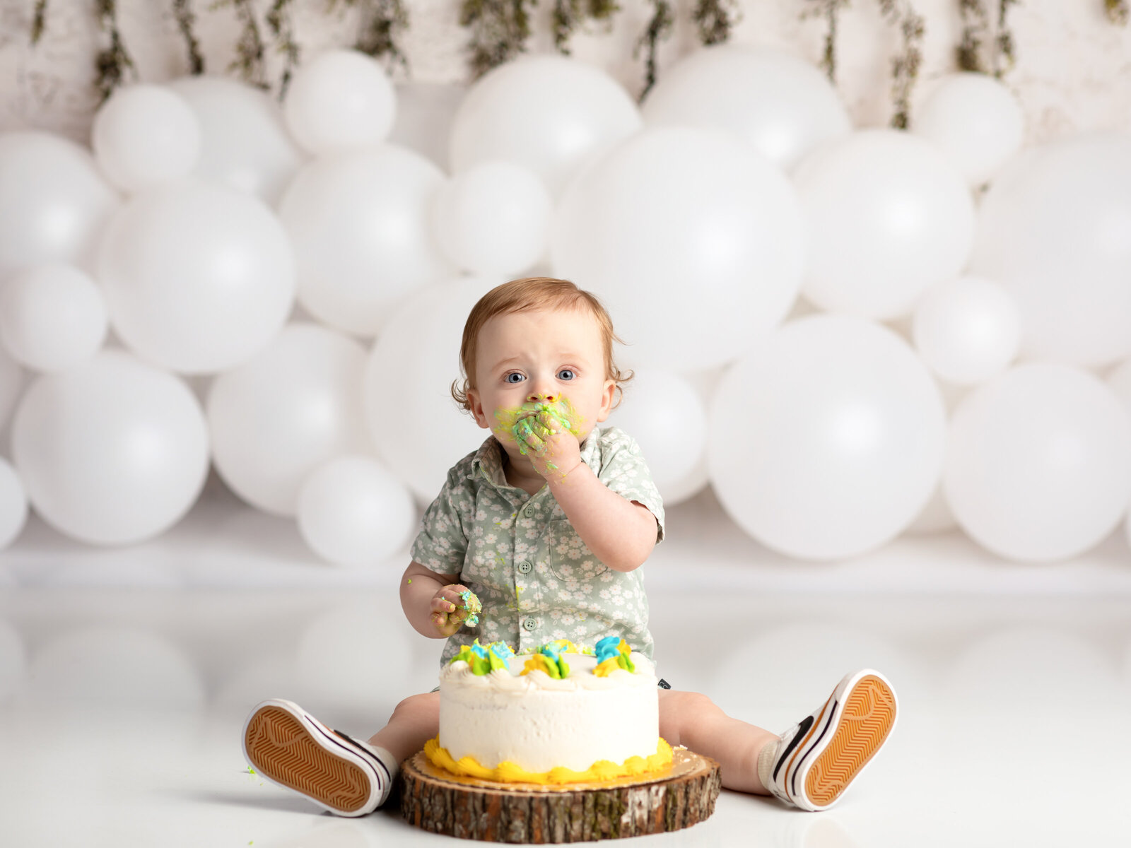 one year old boy eating cake for cake smash photoshoot with white balloon set