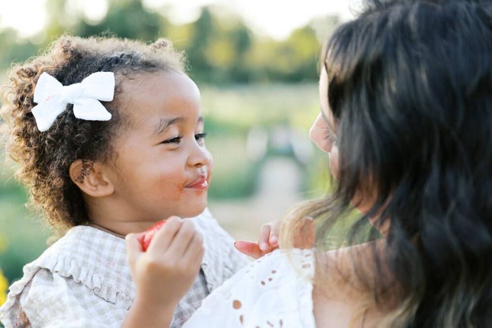 Little girl smiling in her mothers arms eating strawberry taken by Family Photographer Sacramento Kelsey Krall