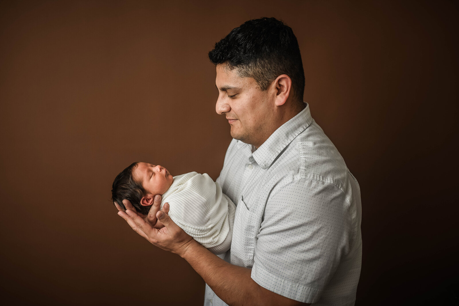 father standing holding  his newborn son in his palms looking at him