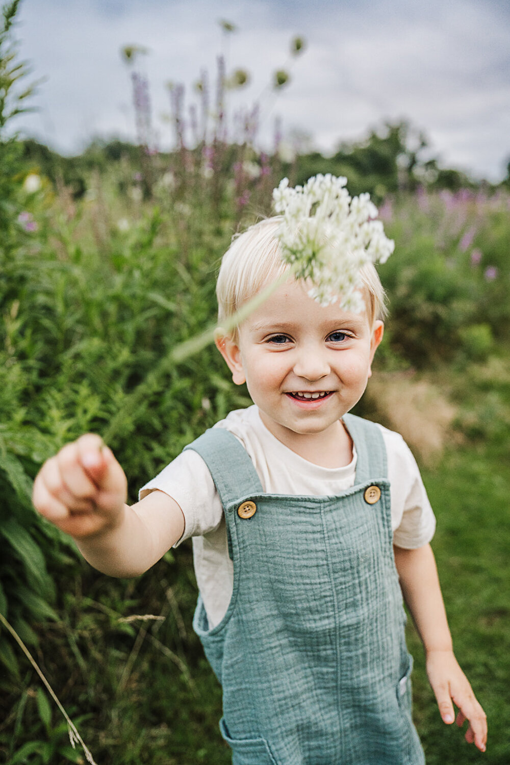 toddler boy waves queen annes lace at camera while smiling
