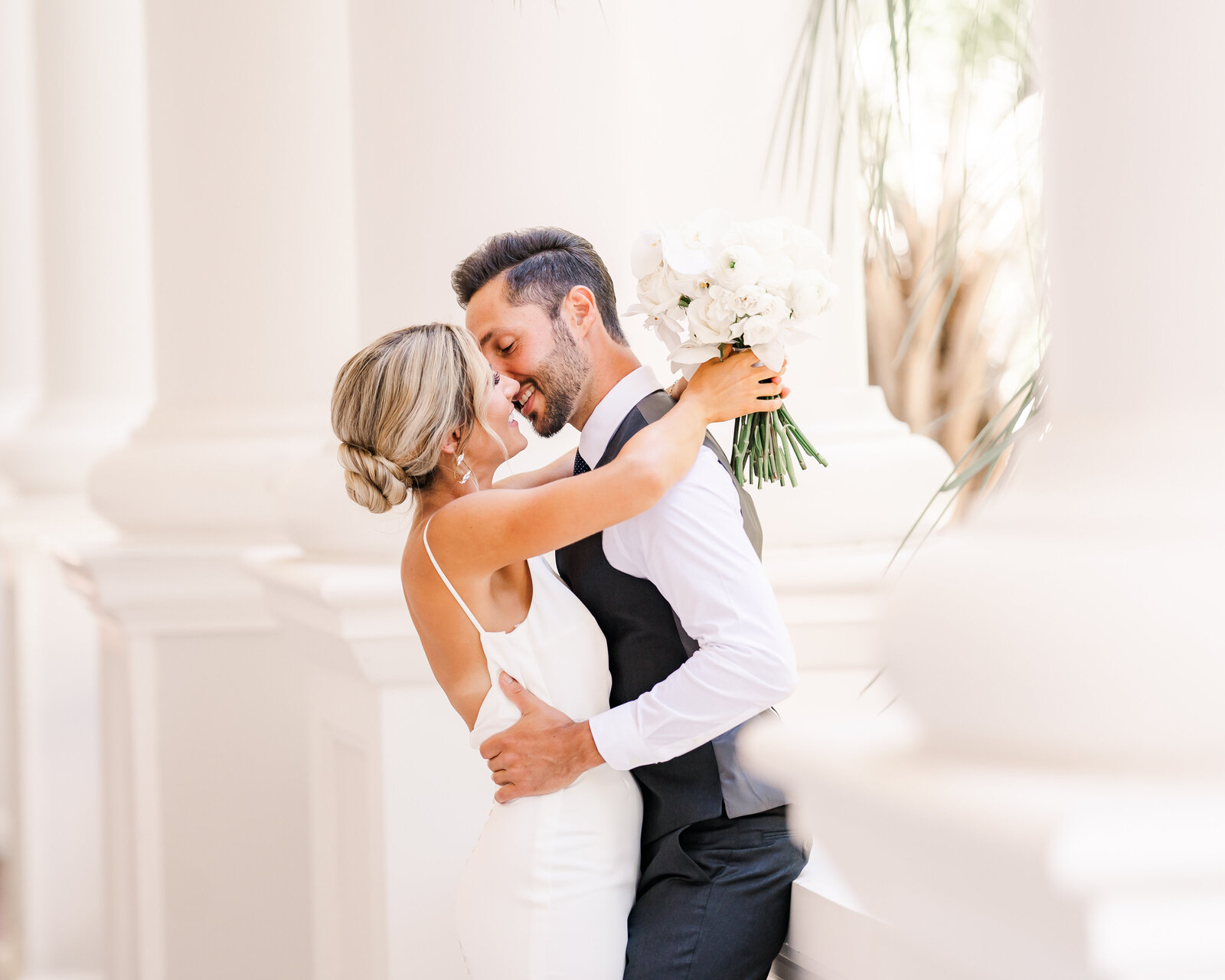 Bride and groom kiss each other next to white columns