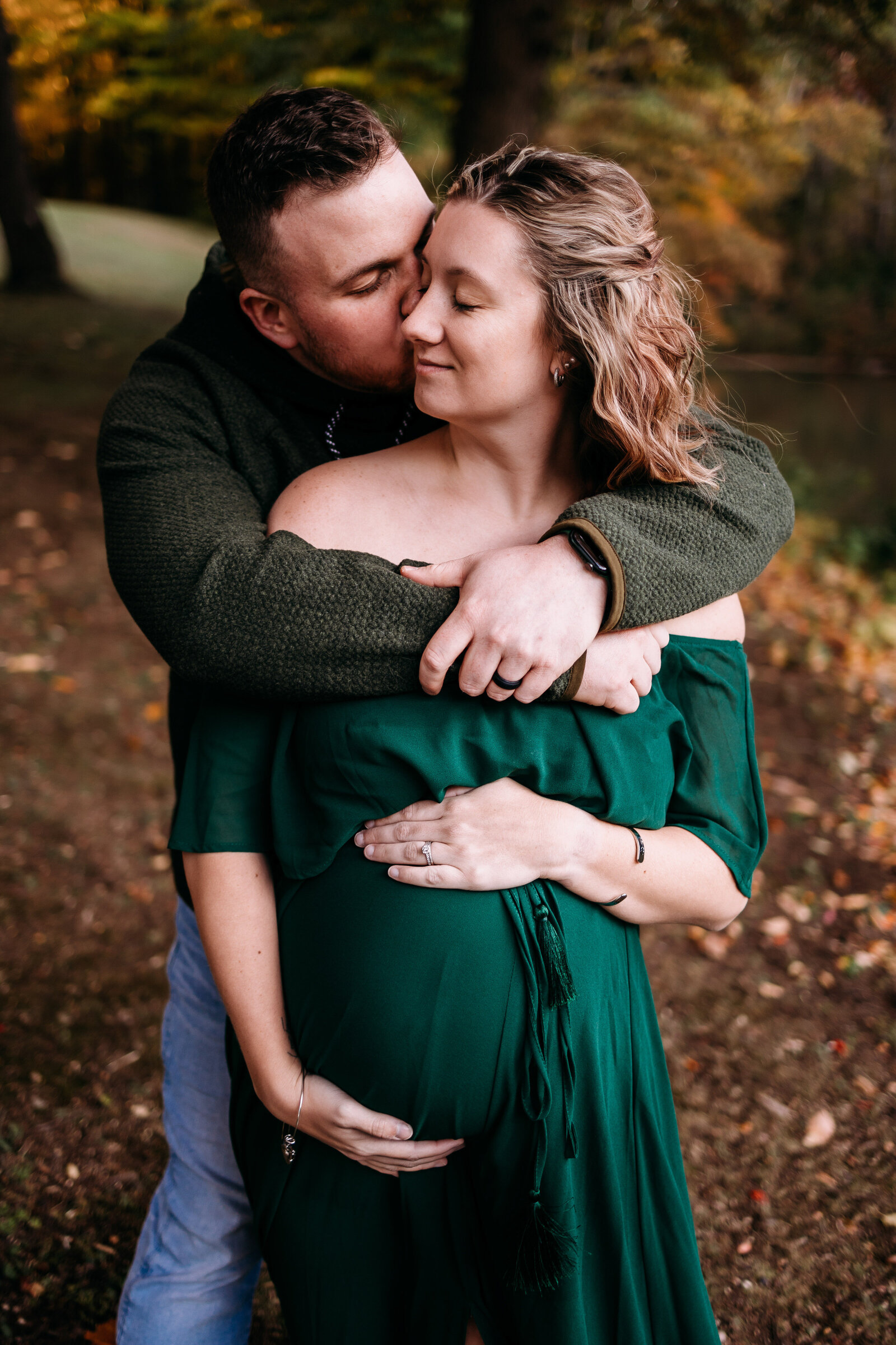 Husband snuggles pregnant wife and gives her a kiss on the cheek during their maternity photography session