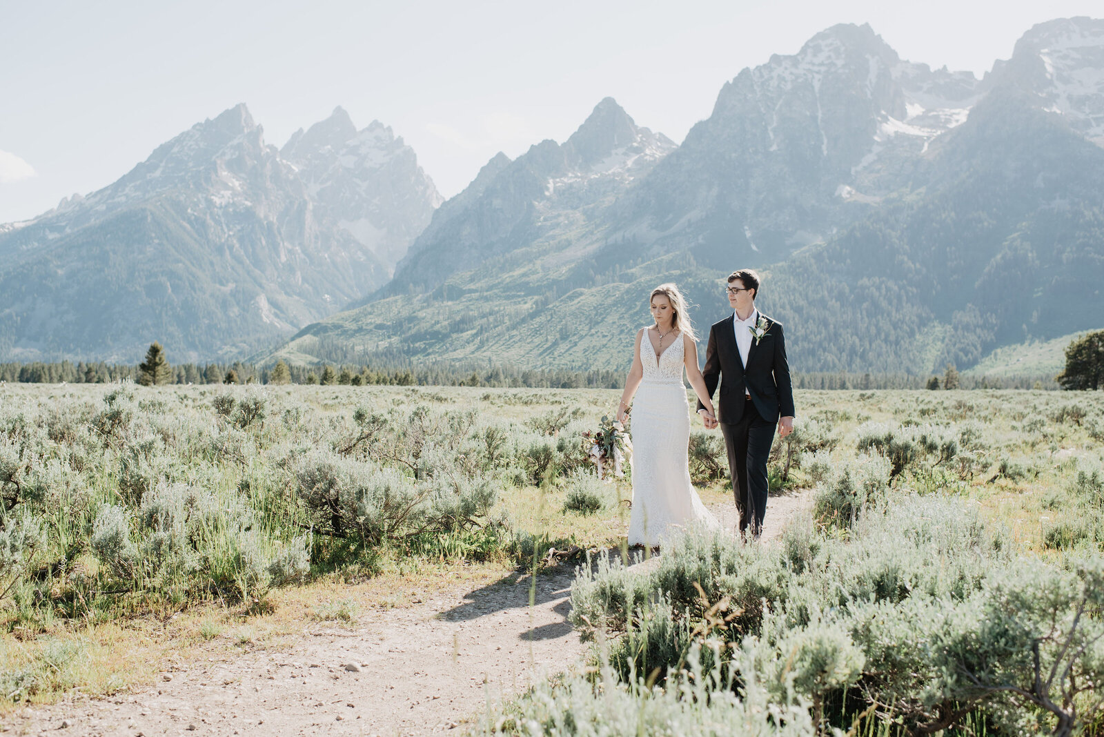 jackson hole wedding locations with close views of the grand tetons for wedding pictures with bride and groom holding hands and wandering through a sage brush field for adventurous elopement photos