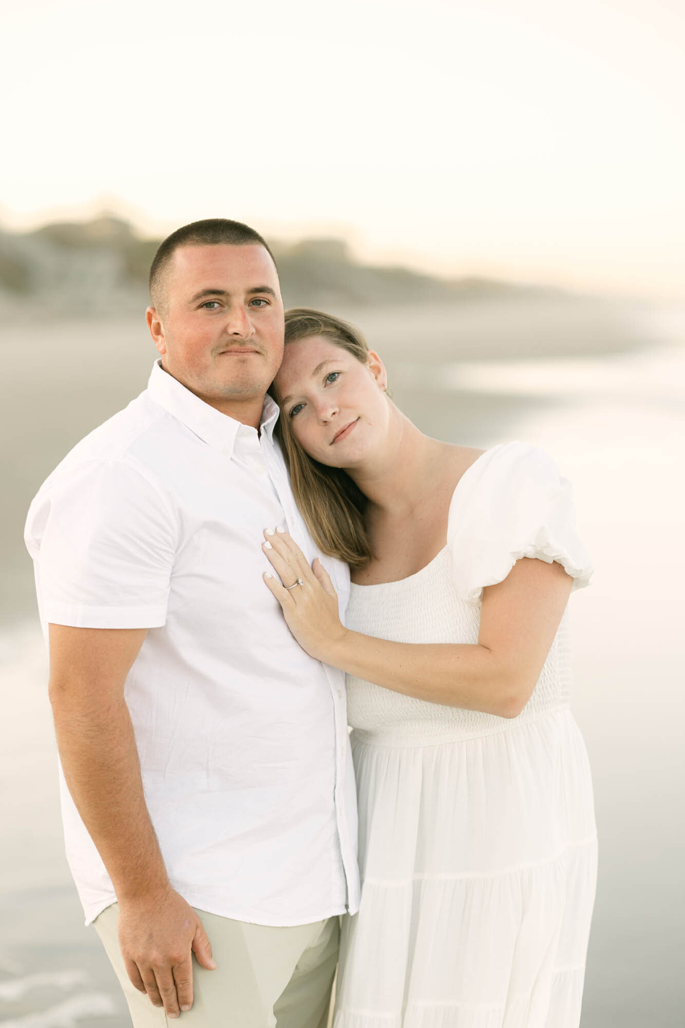 Close-up engagement photo of a couple on the OBX beach looking at the camera