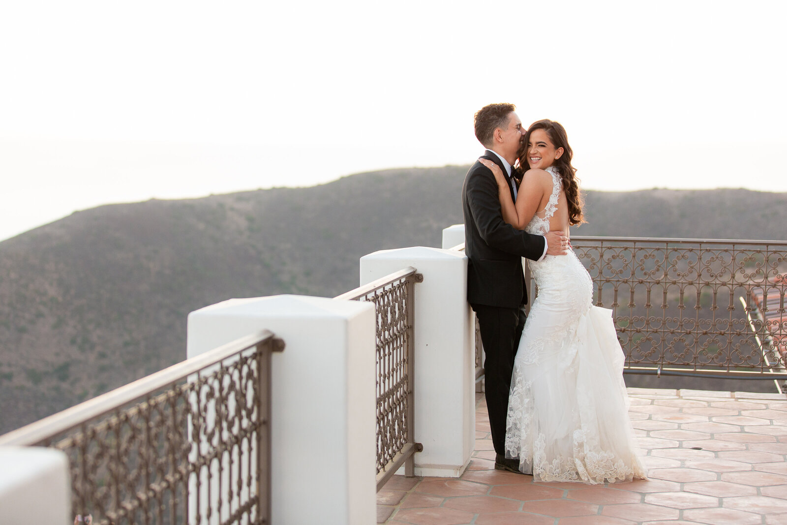 Groom kissing bride while she smiles sweetly overlooking the mountains with Dallas wedding photographer