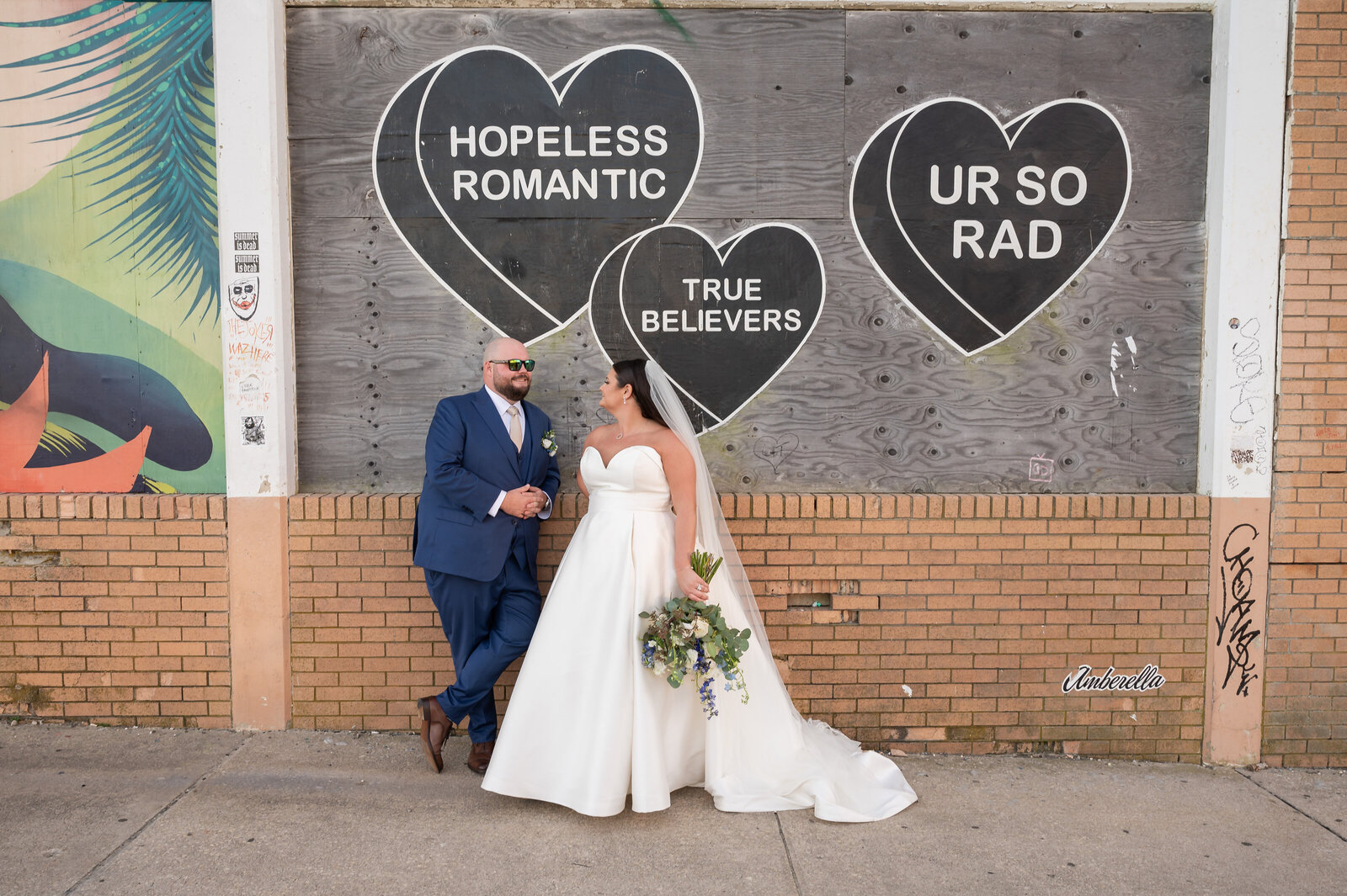 Bride and groom standing in front of a mural on the boardwalk in Asbury Park