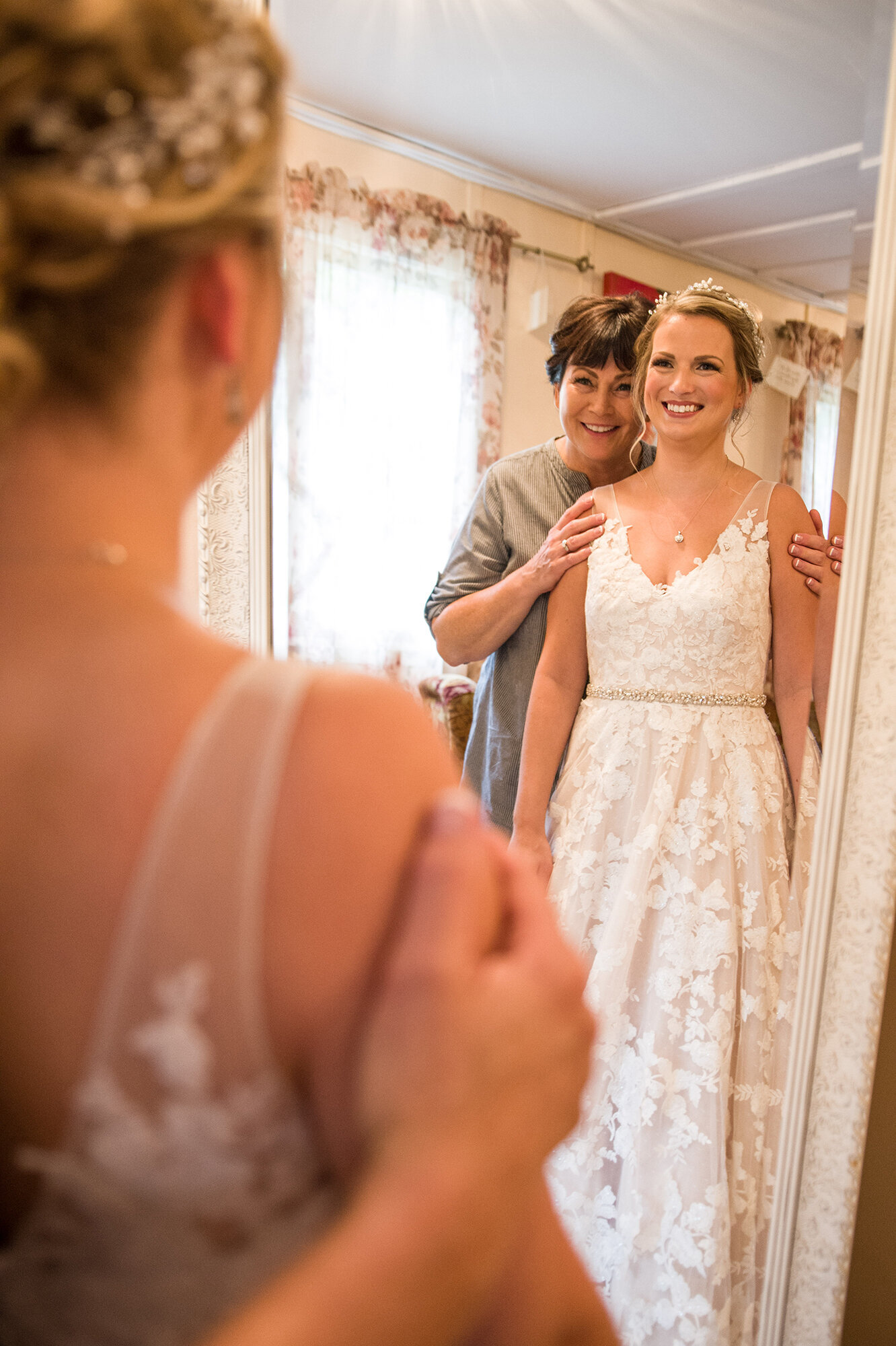 Bride and mom smiling in mirror on wedding day.