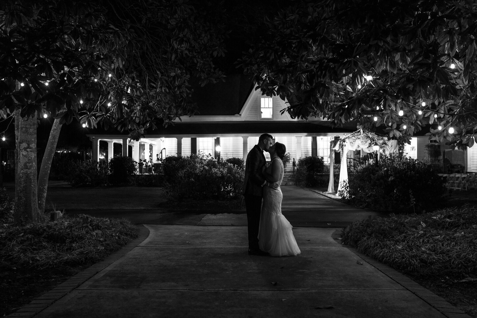 Night time photo of bride & groom kissing backlit by the house.