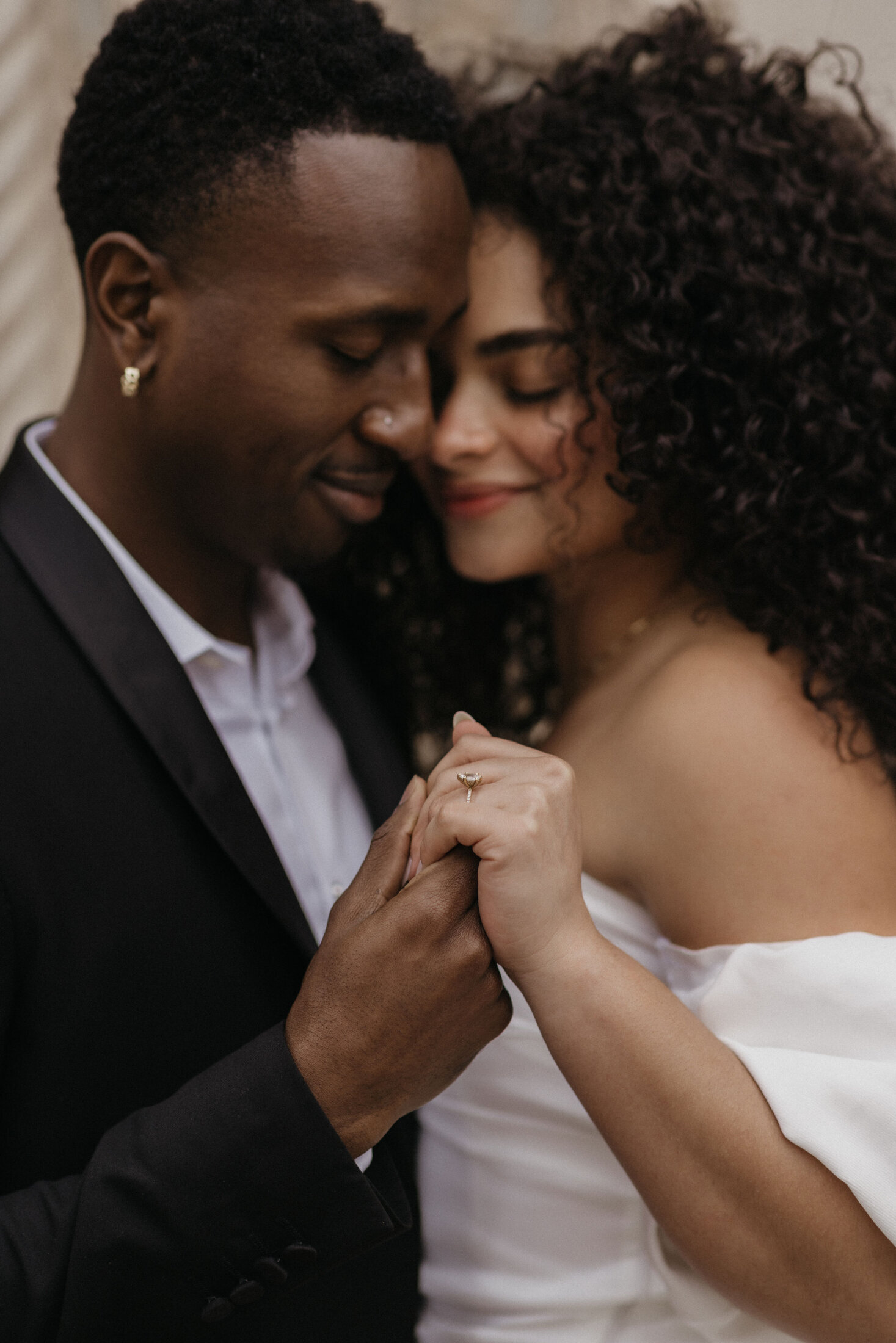 A tender moment during an engagement photoshoot in San Francisco, capturing a  man in a black suit and a woman with curly hair in a white dress, as they hold hands and lean close together