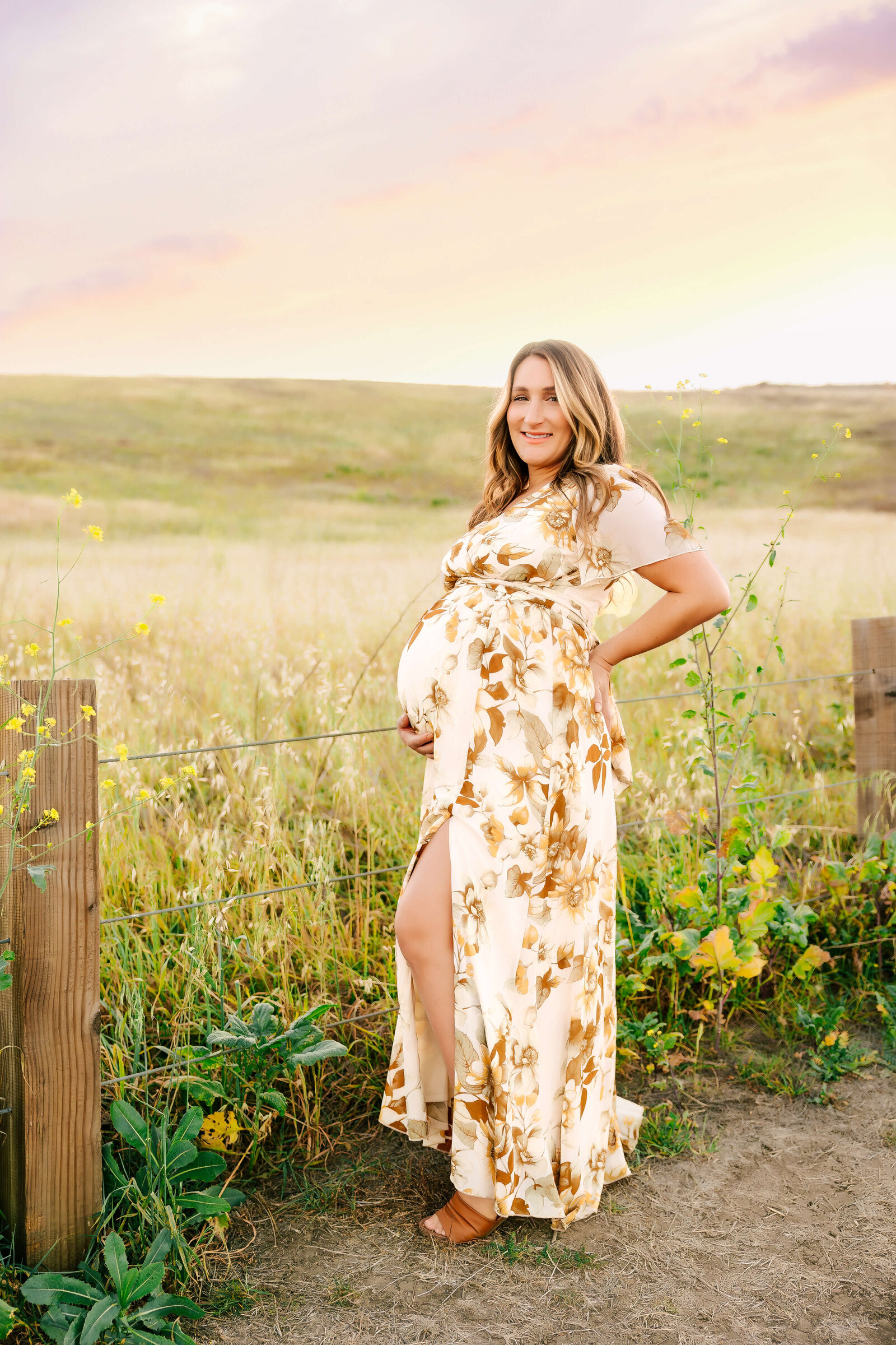 Expectant mom smiling while holding belly in a wildflower field in Irvine by Ashley Nicole.