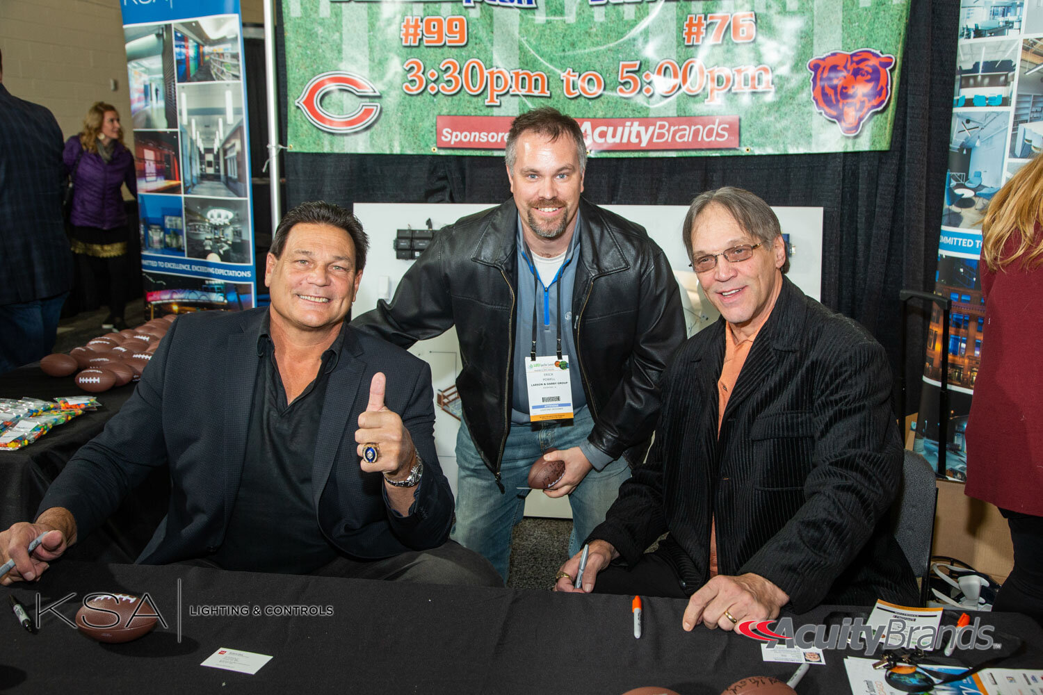 Three men posing at a sports-themed event with signing table