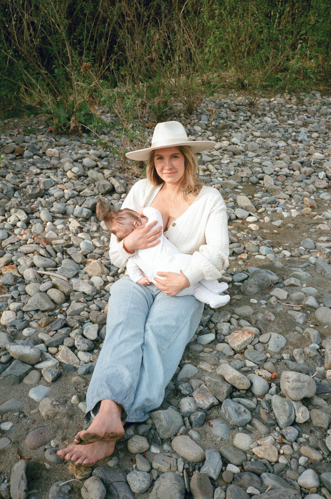 Mother breastfeeding child while sitting on river rocks on the Williamette in Portland, Oregon.