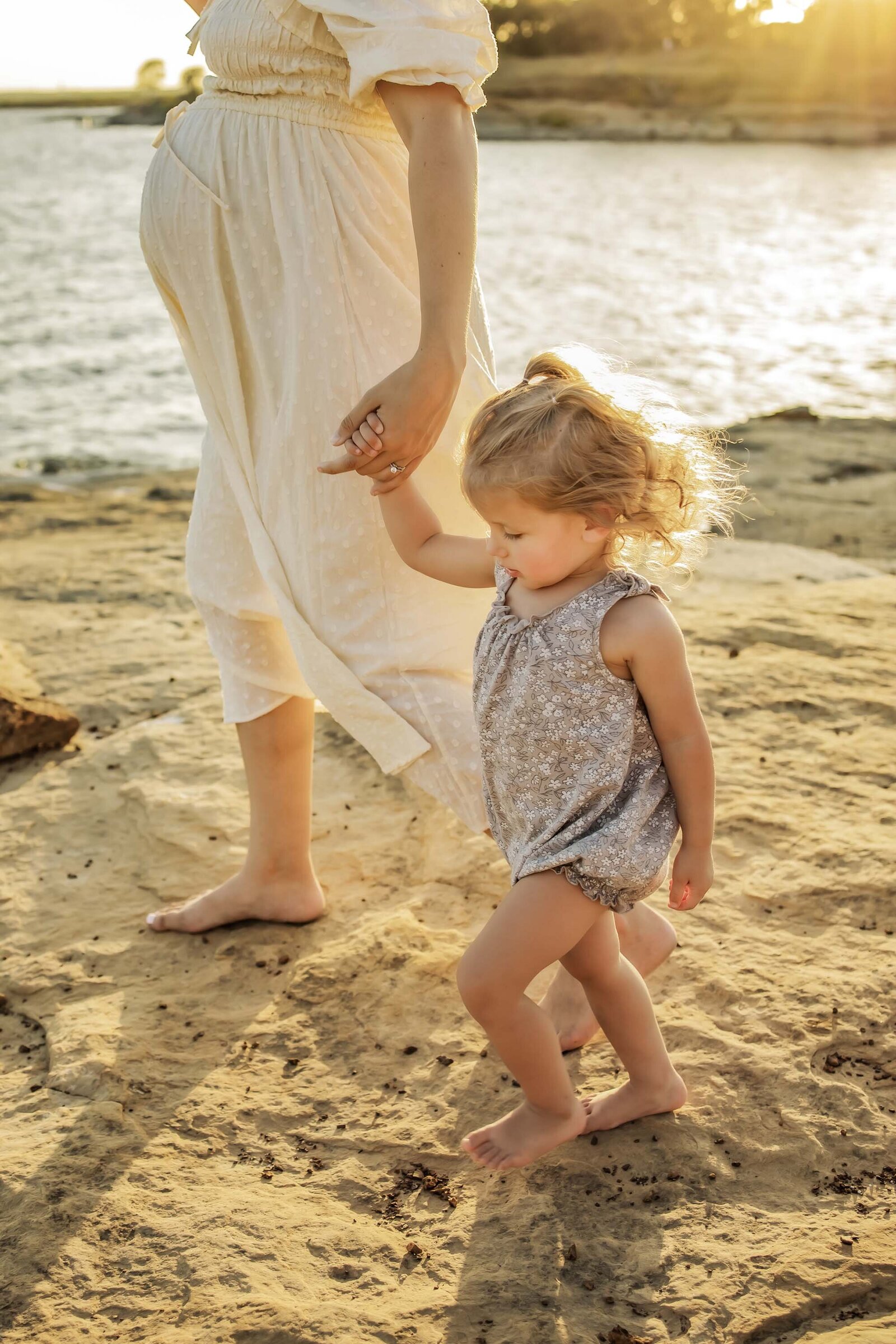 Mom and daughter walk along the water at the lake while at outdoor family portraits at golden hour in Flower Mound Texas