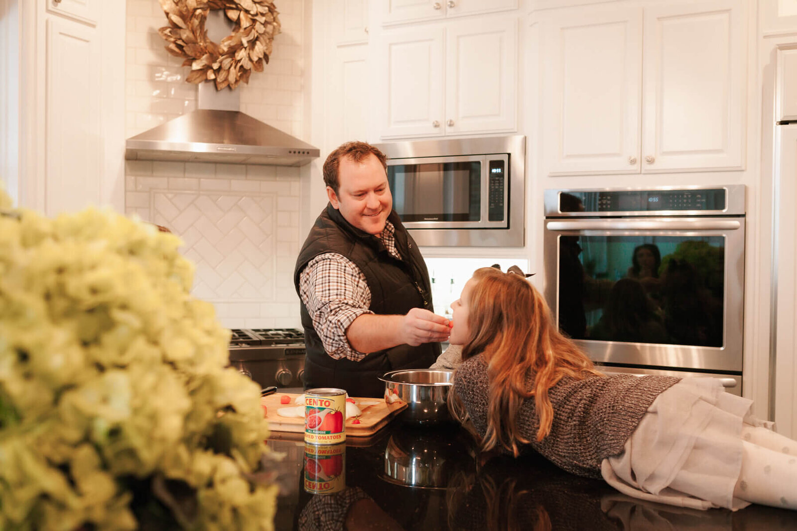 A daddy gives his daughter a sample of dinner as he's cooking.